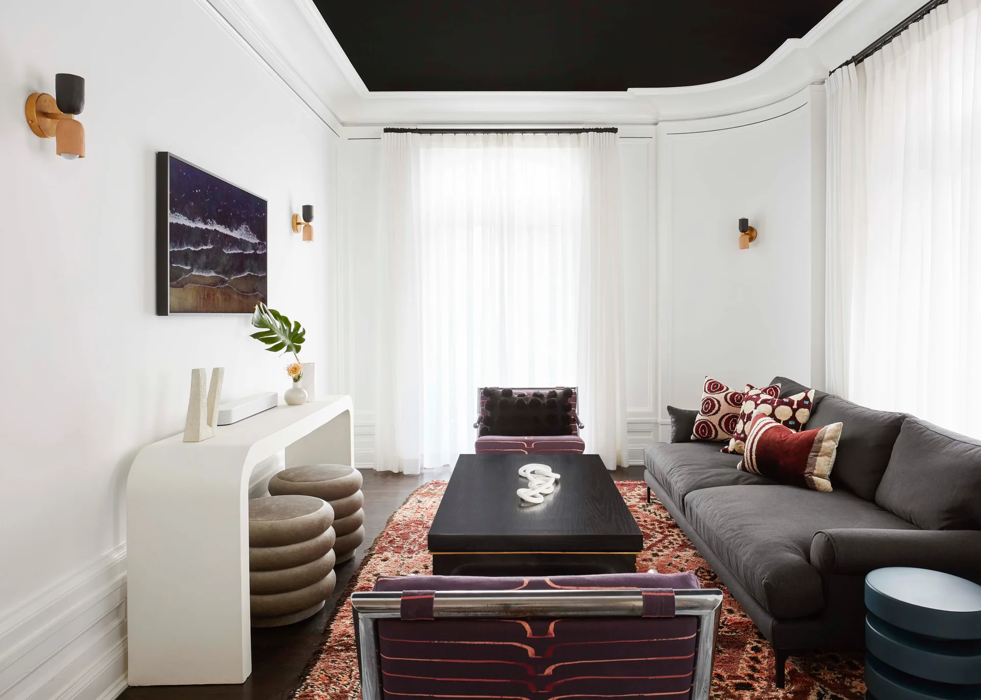 A high-contrast living room features a dark charcoal sofa, a black painted ceiling, white walls with trim, and a curved white console table.