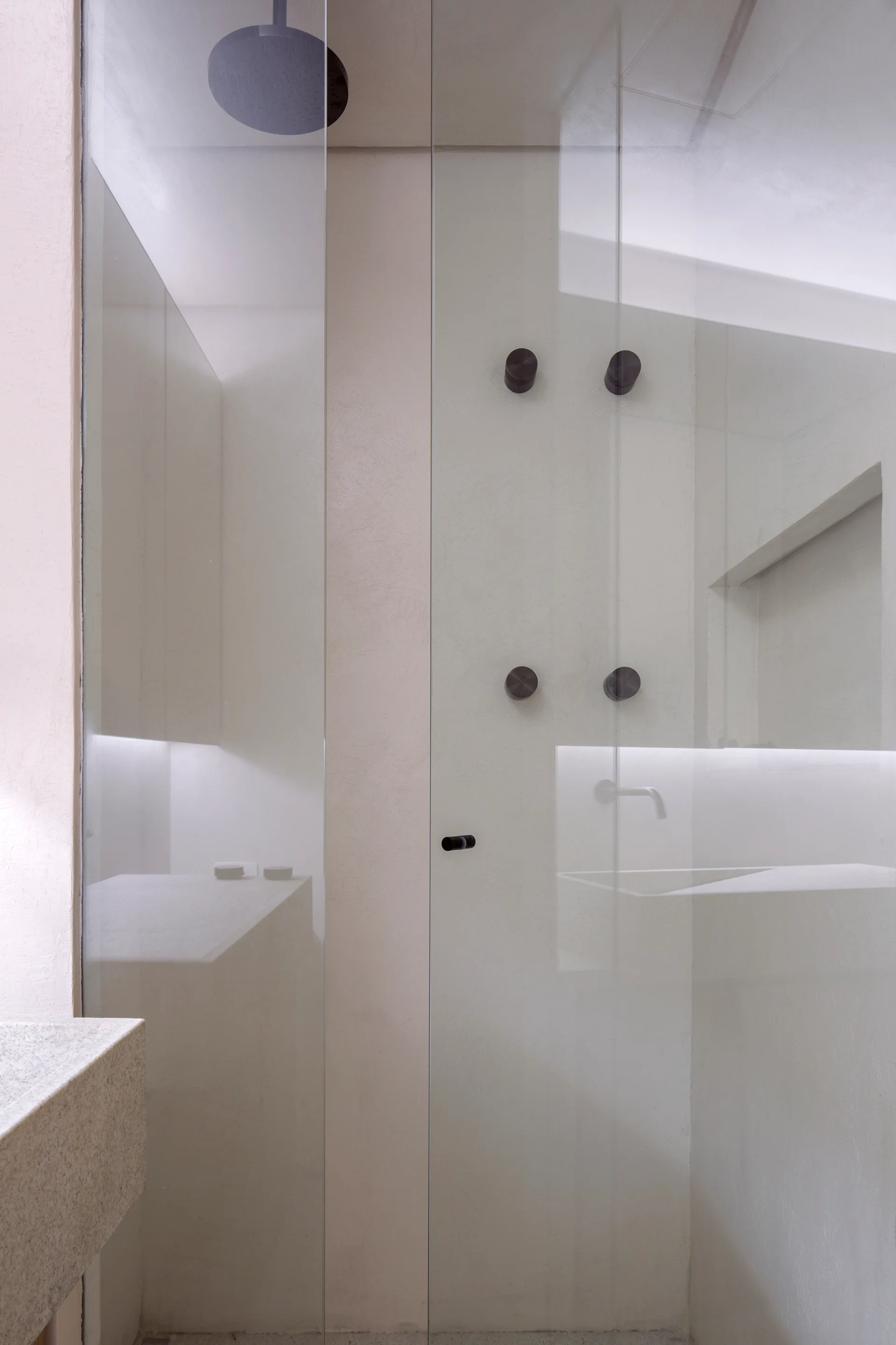 A minimalist walk-in glass shower features matte black hardware, smooth off-white plaster walls, and a recessed glowing light strip.