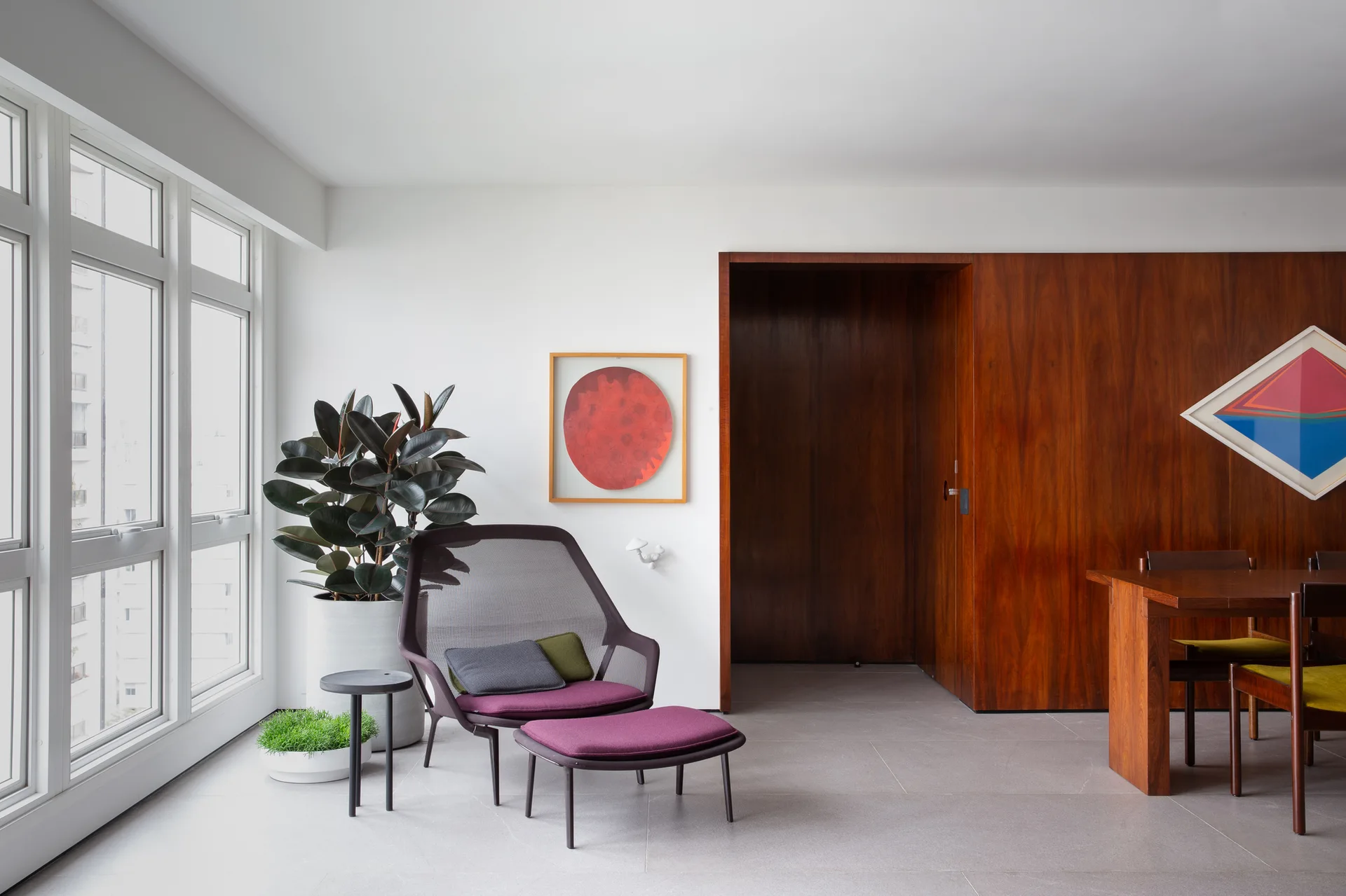 A minimalist living space features a purple mesh lounge chair and matching ottoman near a large window, next to a rich wood paneled accent wall.