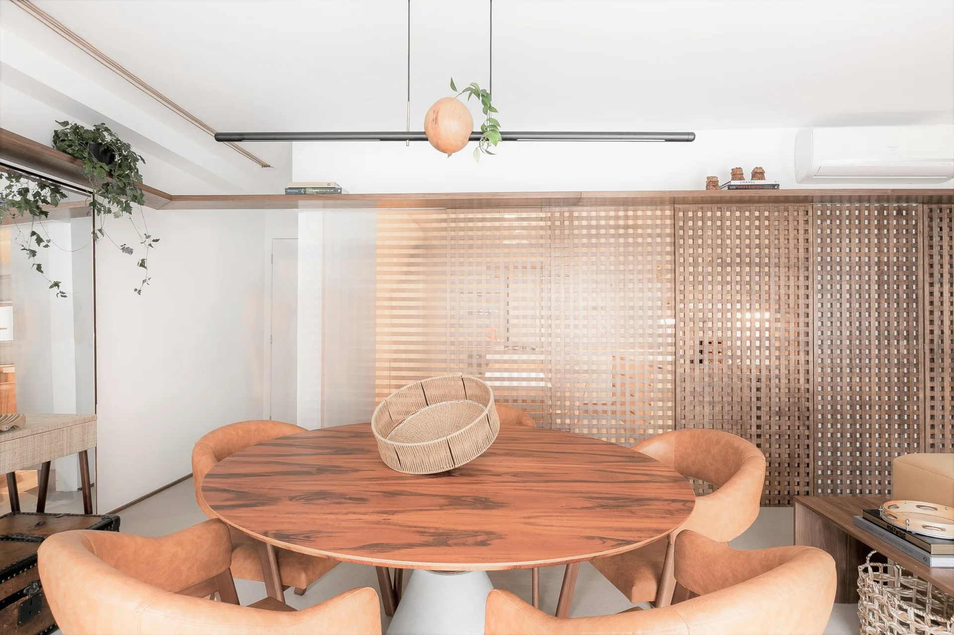 A round wooden dining table surrounded by tan curved armchairs stands in front of a wooden lattice room divider screen.