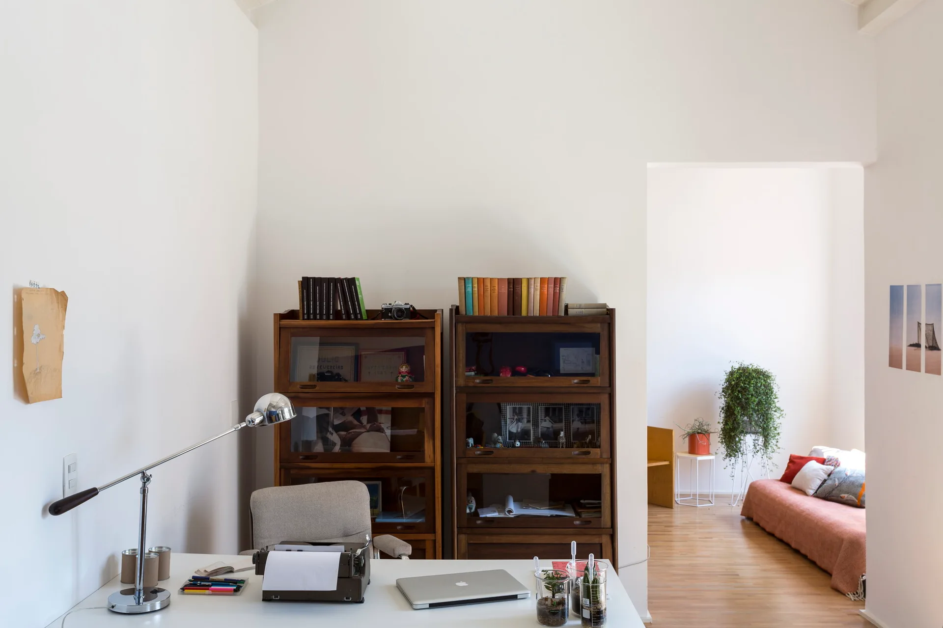 A white home office featuring a desk with a vintage typewriter and laptop, positioned in front of two glass-front wooden bookcases.