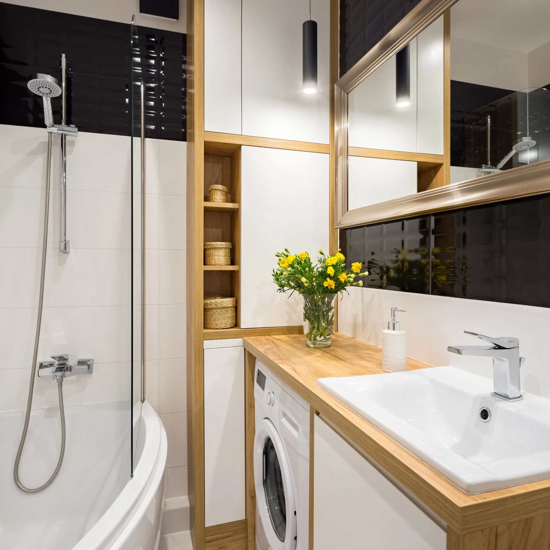 A contemporary bathroom features a white sink on a wood countertop with an integrated washing machine next to a bathtub with a glass screen.