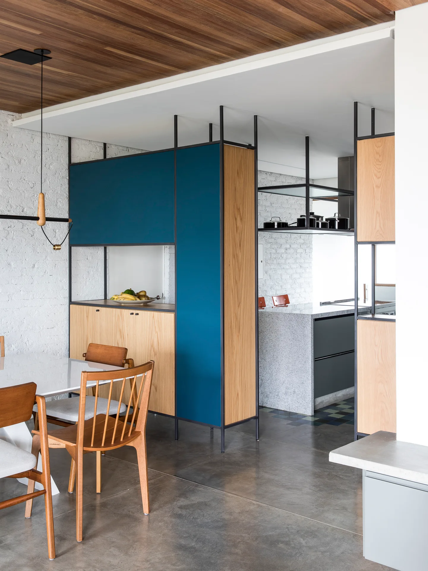 A dining space next to a kitchen featuring a teal and wood room-divider cabinet, wooden table and chairs, and a painted white brick wall.