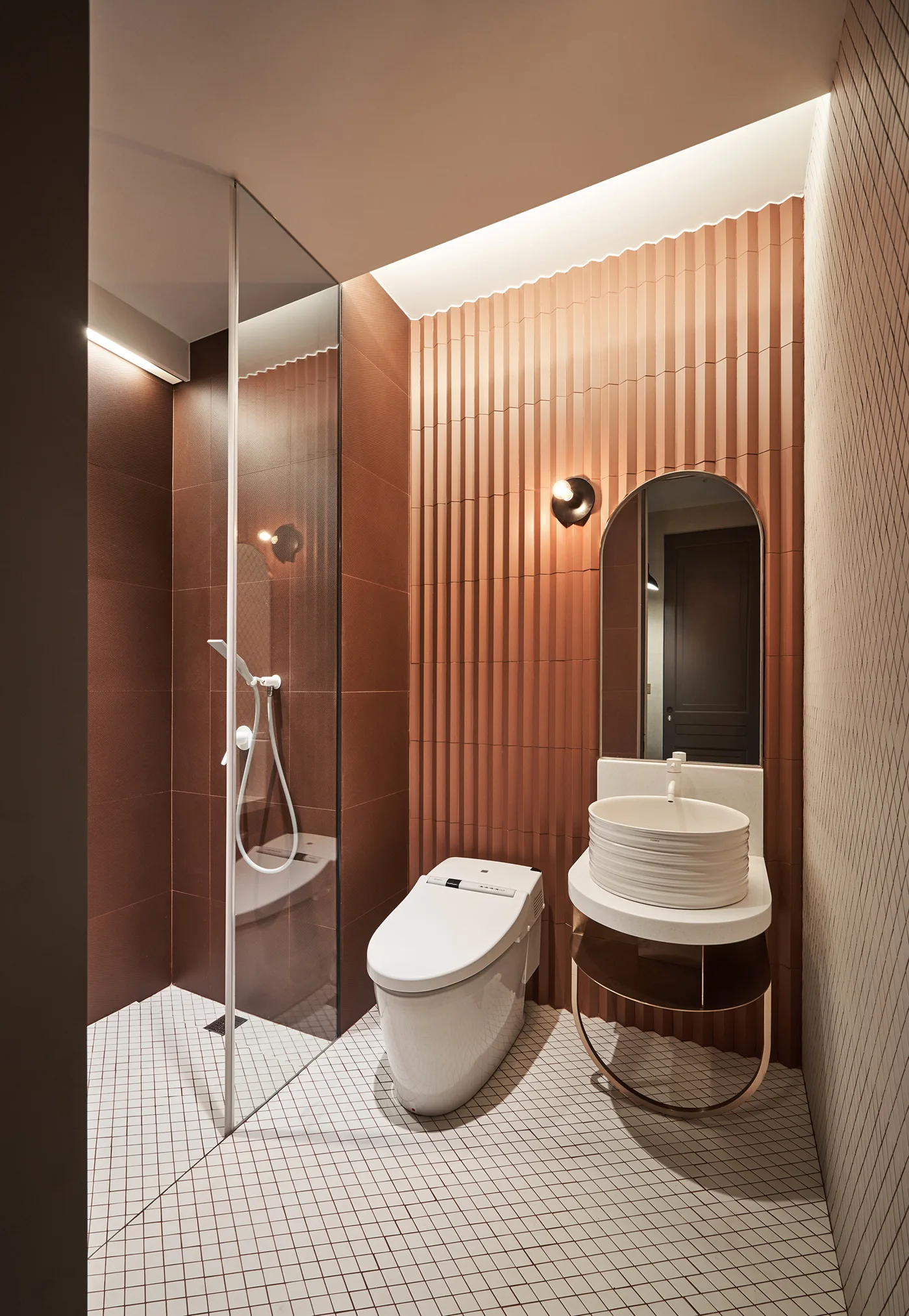 A modern bathroom features textured terracotta fluted wall tiles, a white grid tile floor, a glass shower stall, and a white vessel sink vanity.