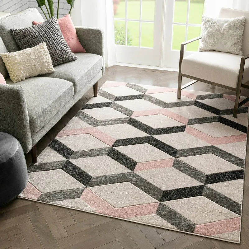 A modern living room features a grey sofa and cream armchair arranged on a pink and grey geometric cube patterned rug over herringbone wood floors.