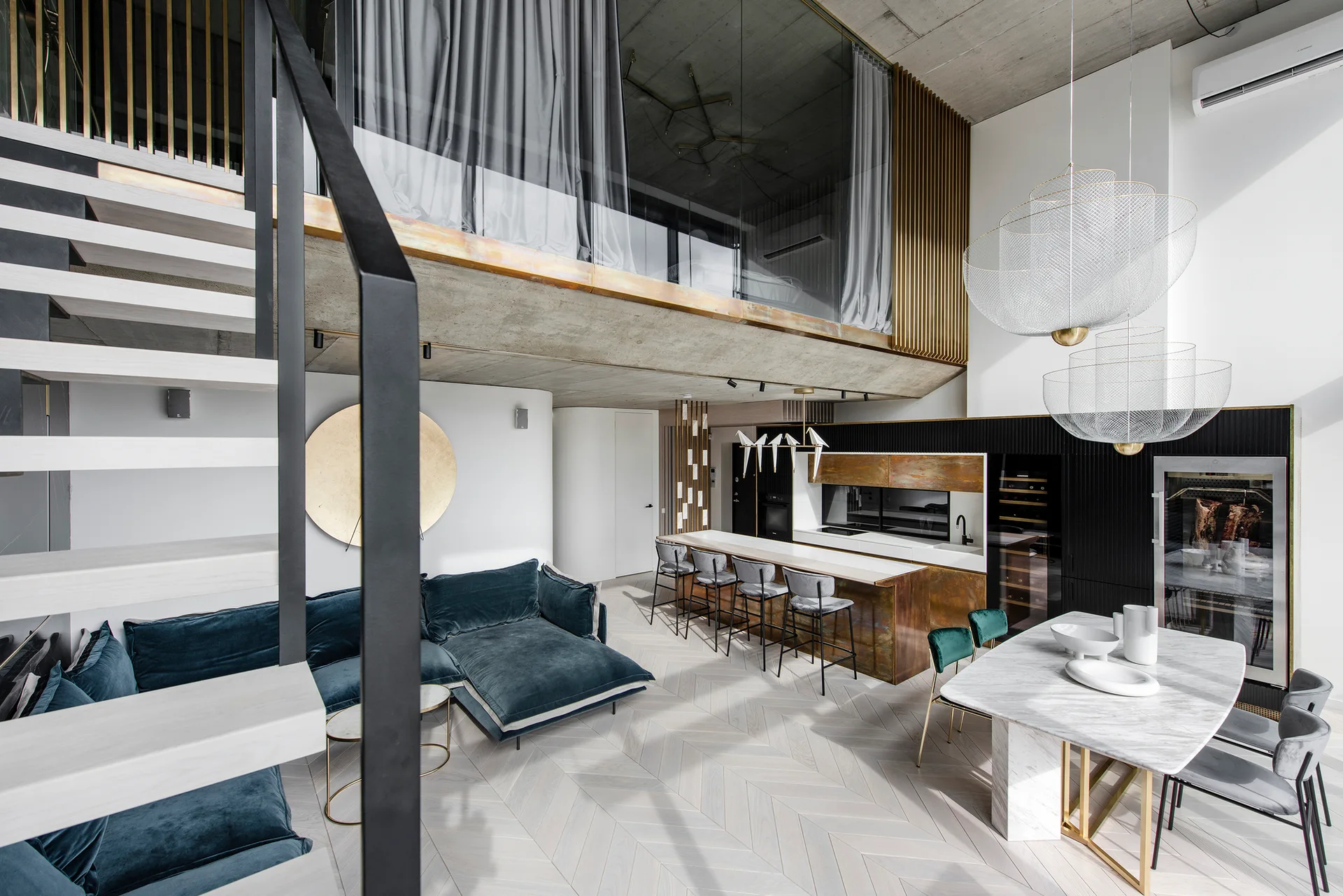 A modern open-plan loft featuring a blue velvet sectional sofa, a marble dining table with mesh pendant lights, and a kitchen with copper cabinetry.