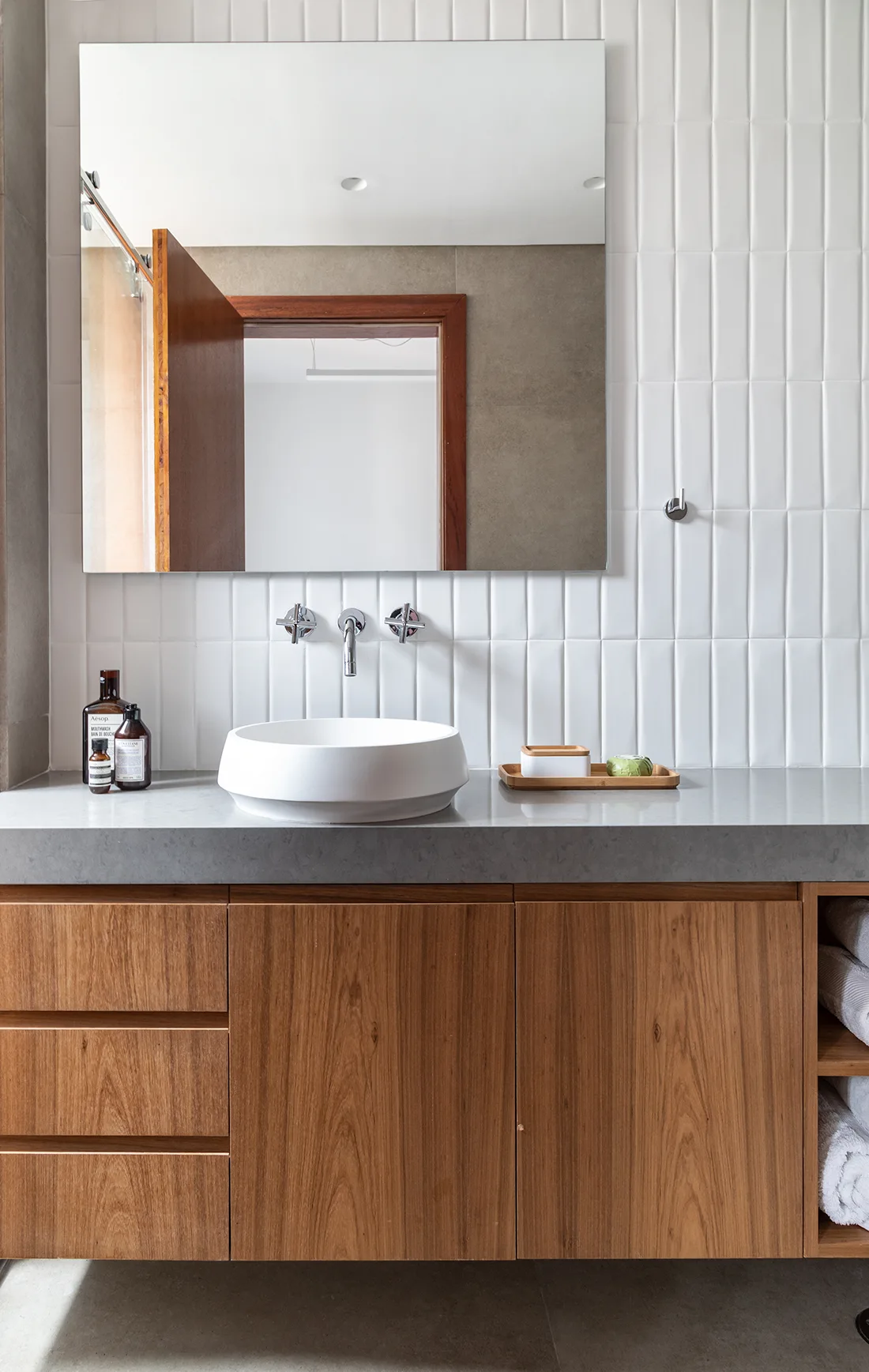 A modern bathroom vanity featuring a wood grain cabinet, a gray stone countertop, a white vessel sink, and a vertical white tile backsplash.