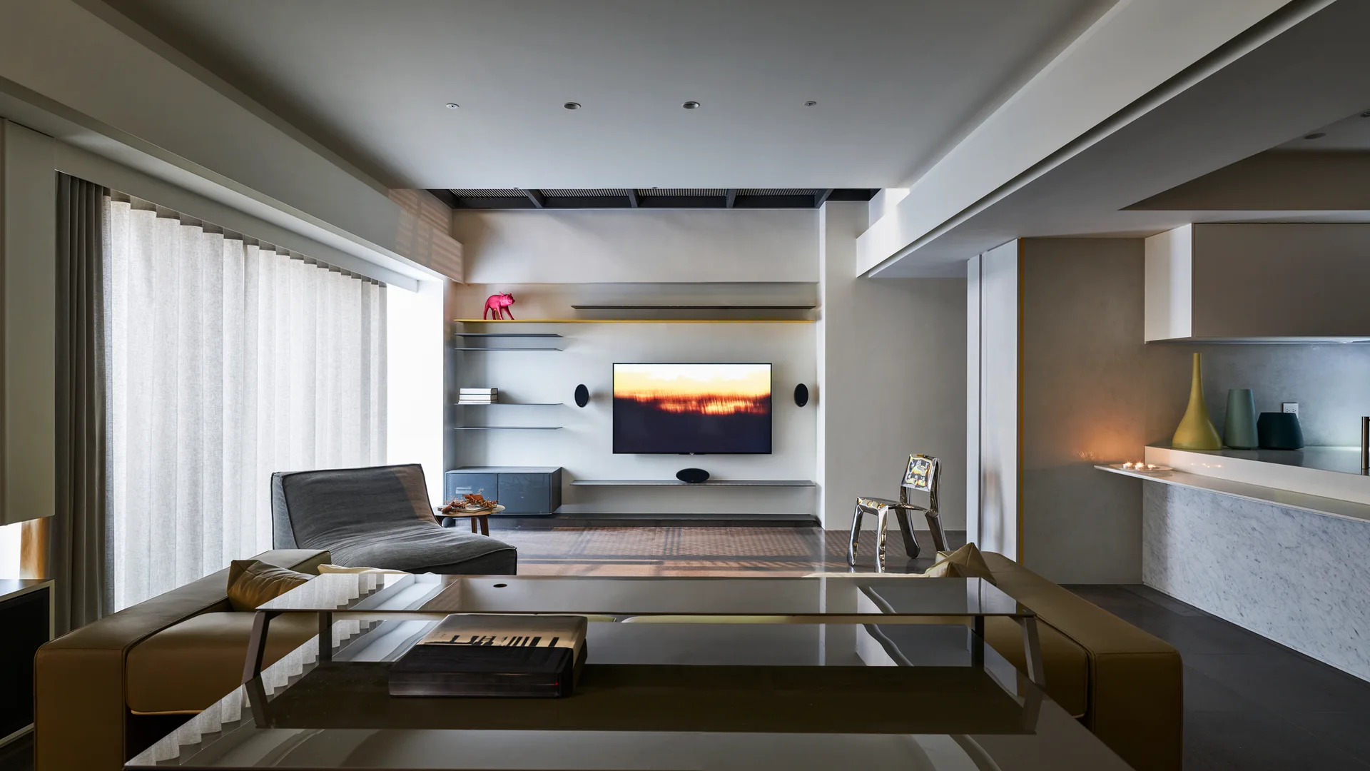 A minimalist living room features a wall-mounted television, thin floating shelves, a tan leather sofa, and a sculptural metallic accent chair.