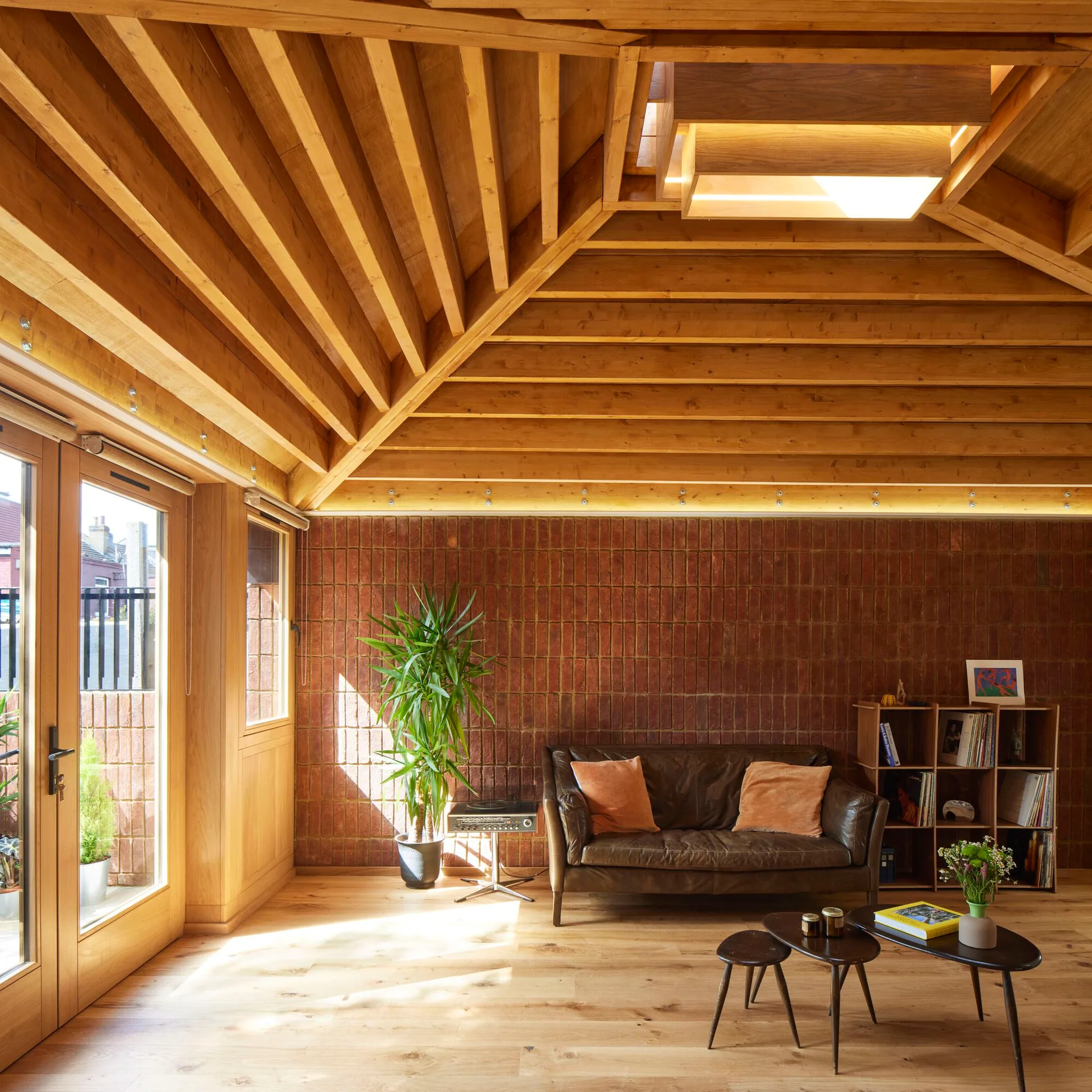 A bright living room with a vaulted wood ceiling, an exposed red brick wall, and a brown leather sofa with orange pillows.