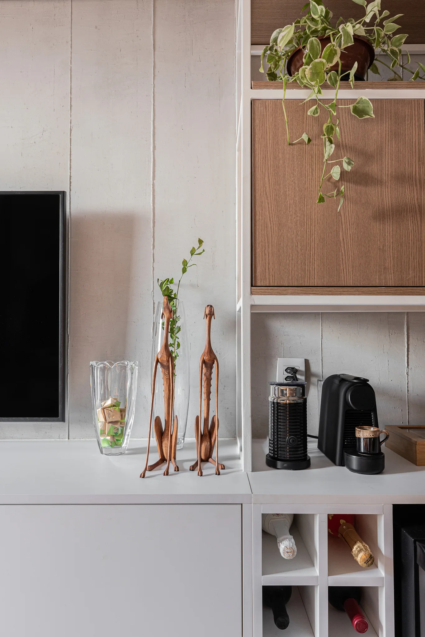A white built-in cabinet featuring a black coffee maker, wooden dog sculptures, wine cubbies, and an upper cabinet with a wood-grain door.