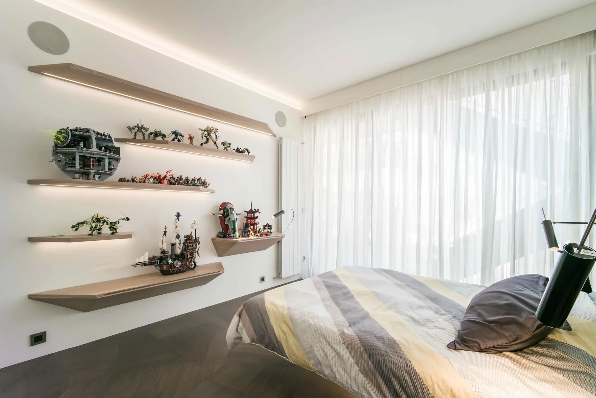 Wood-toned floating shelves with integrated LED lights display collectible model toys on a white wall in a modern bedroom.