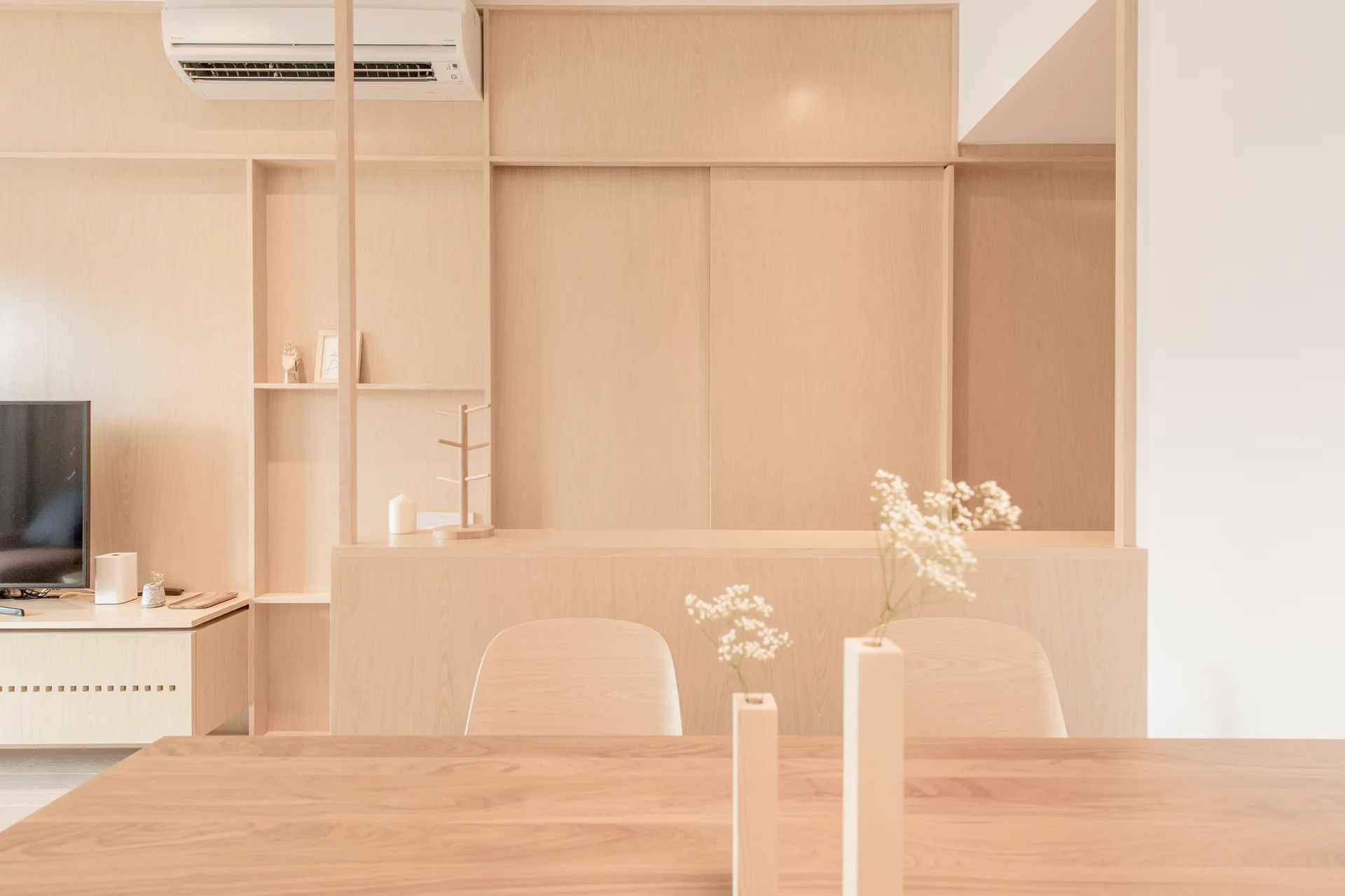 A light wood dining table with two bud vases sits in front of two wooden chairs and a massive custom built-in wood cabinet system.