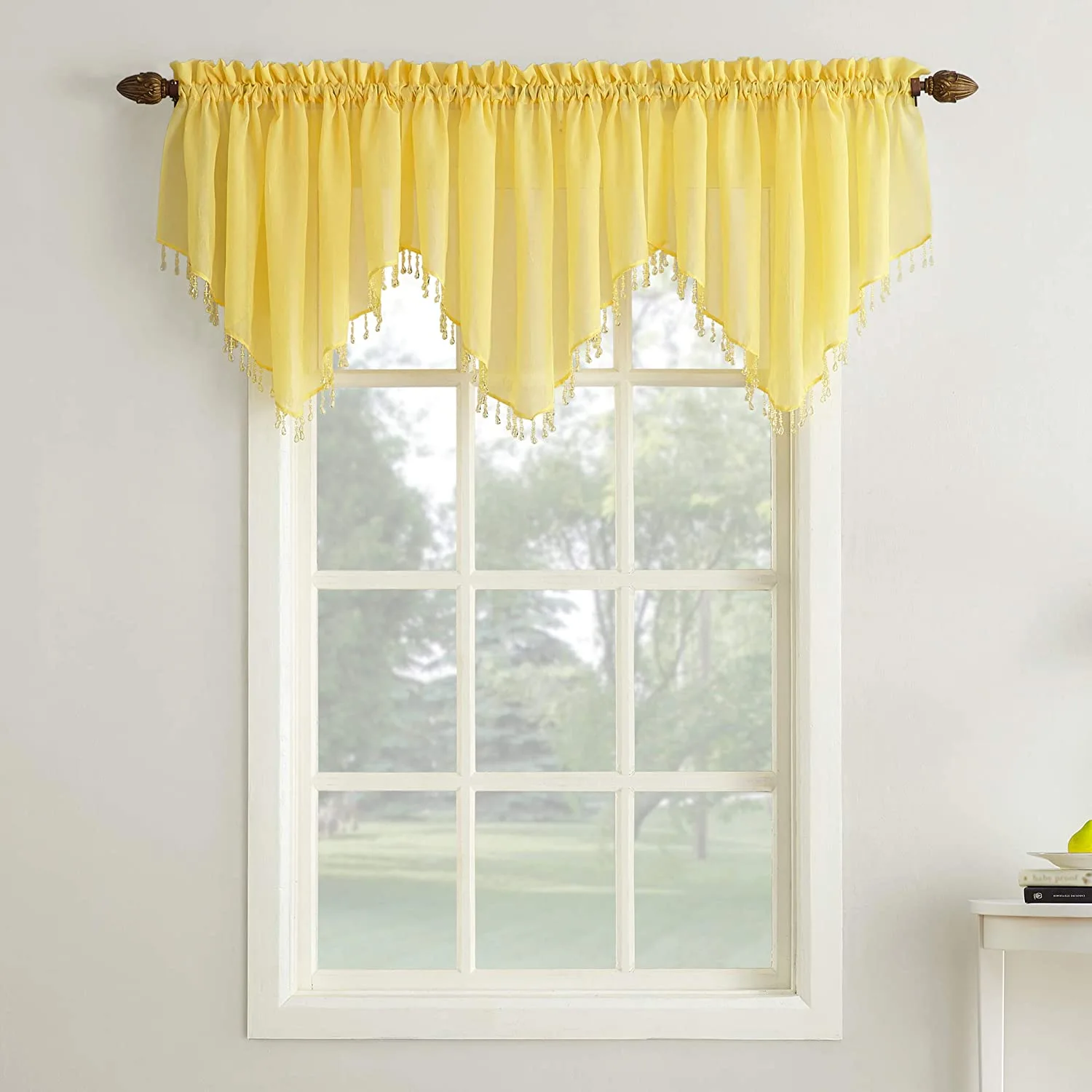 A bright yellow sheer valance with beaded scalloped edges hangs over a white framed window.