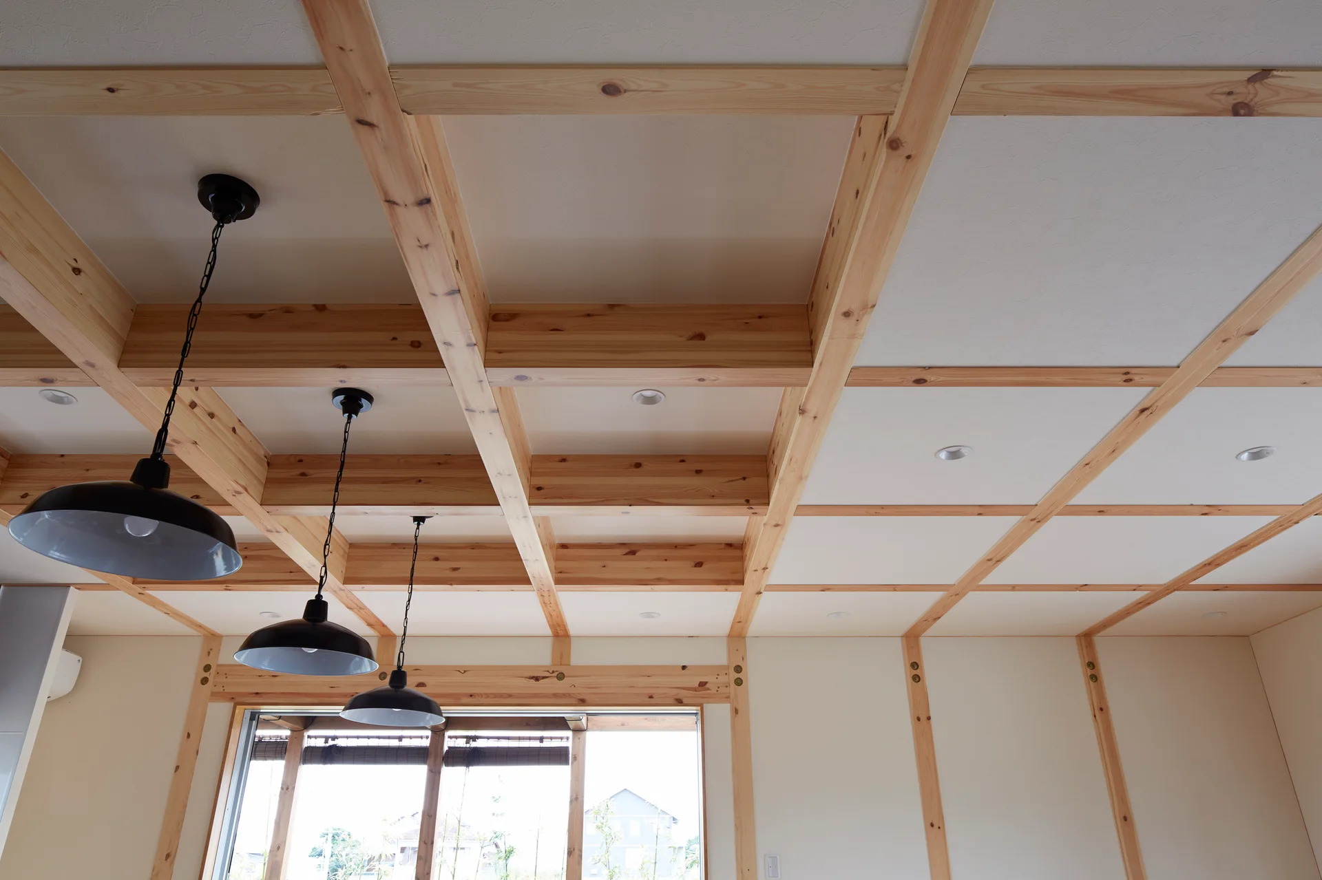 A natural wood grid ceiling features embedded recessed lighting and three black metal pendant lights hanging over an off-white room.