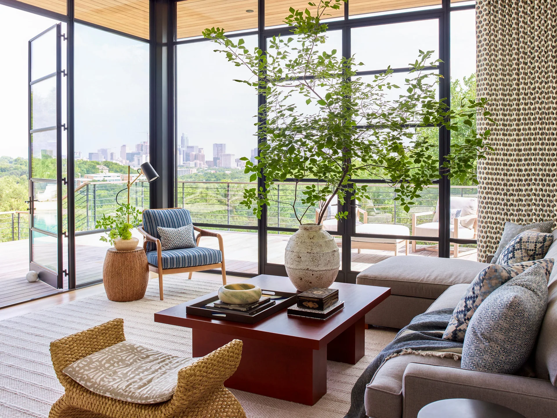 A contemporary living room featuring a grey sectional, a blue striped armchair, a wood plank ceiling, and floor-to-ceiling glass doors opening to a terrace.