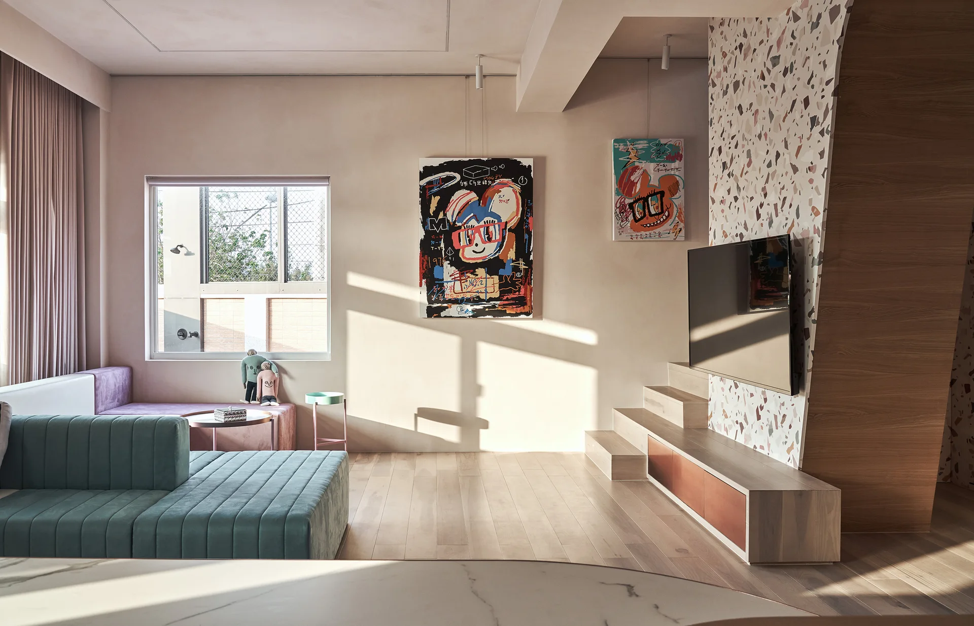 A contemporary living room featuring a teal sectional sofa, a light wood stepped platform, and a television mounted on a speckled terrazzo accent wall.