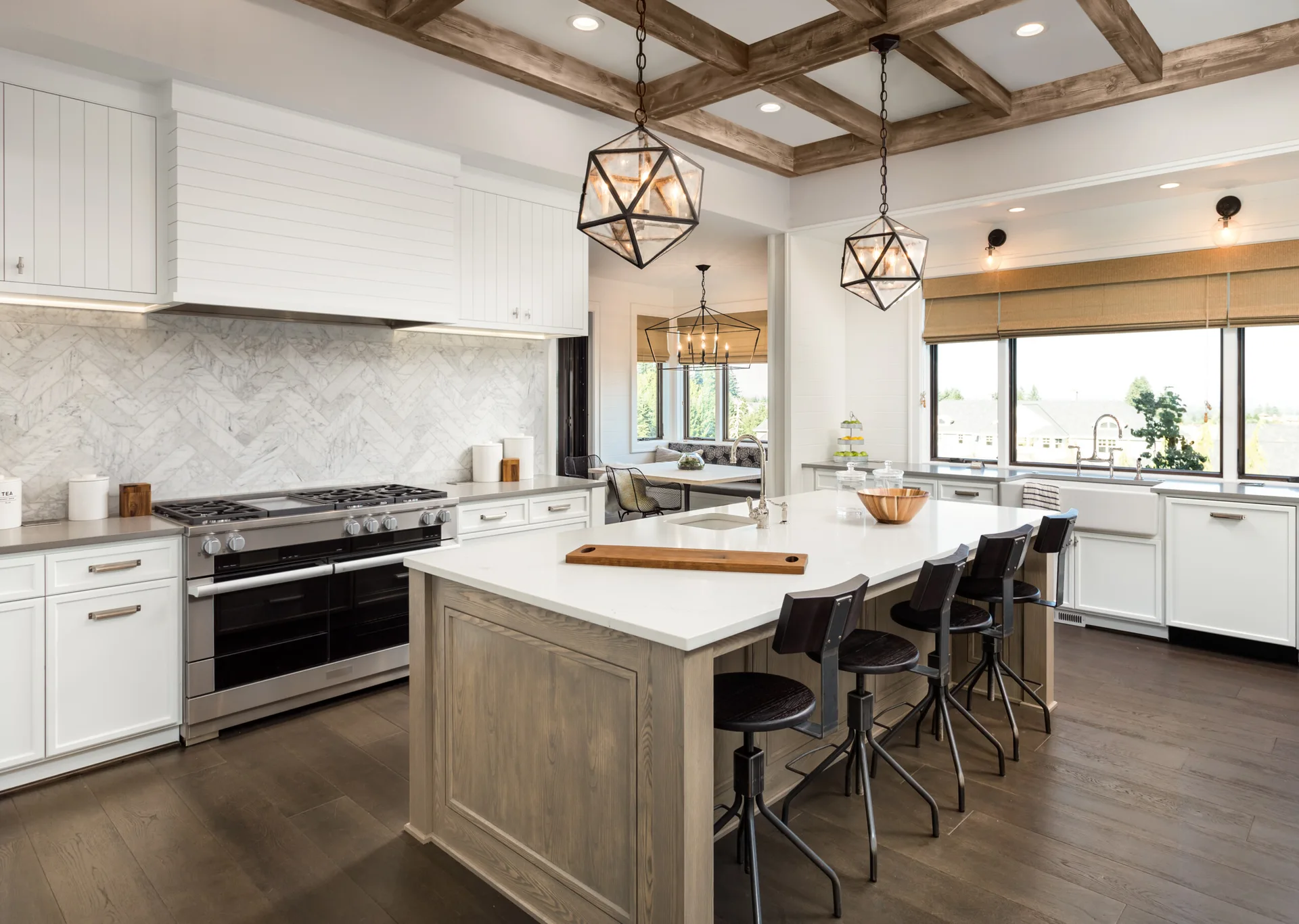 A transitional kitchen with a white-countertop island, dark swivel stools, a herringbone tile backsplash, and decorative wooden ceiling beams.