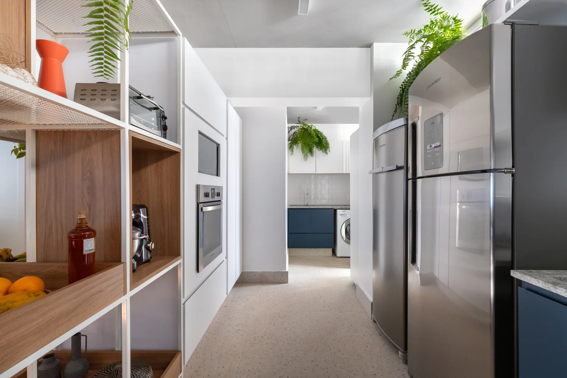 A modern galley kitchen features seamless white cabinets with built-in appliances, stainless steel refrigerators, and open metal shelving with wood inserts.