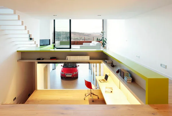 A modern split-level interior featuring a built-in wooden desk, a red chair, white floating stairs, and a bright lime green ledge.