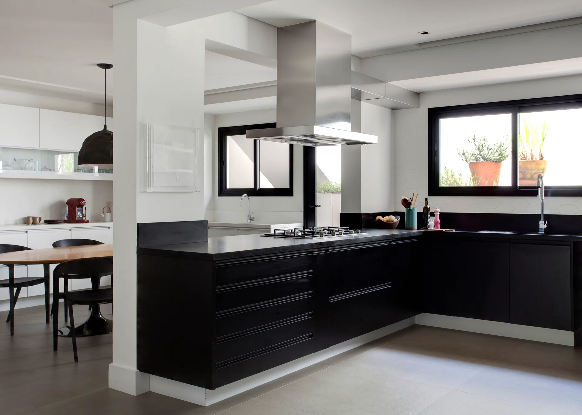 A modern kitchen featuring matte black lower cabinets, a stainless steel range hood, black-framed windows, and an adjacent dining area.