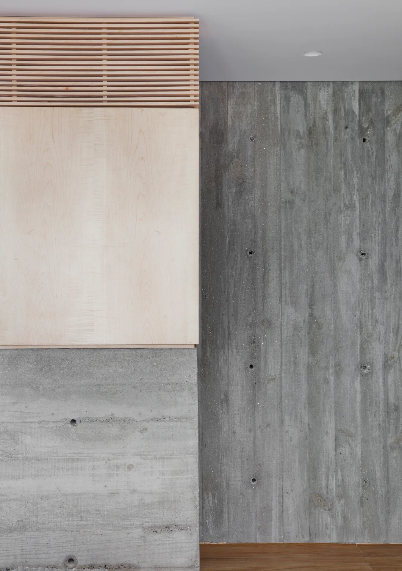 A minimalist wall featuring textured board-formed grey concrete panels alongside a smooth blonde wood cabinet and matching horizontal wood slat details.