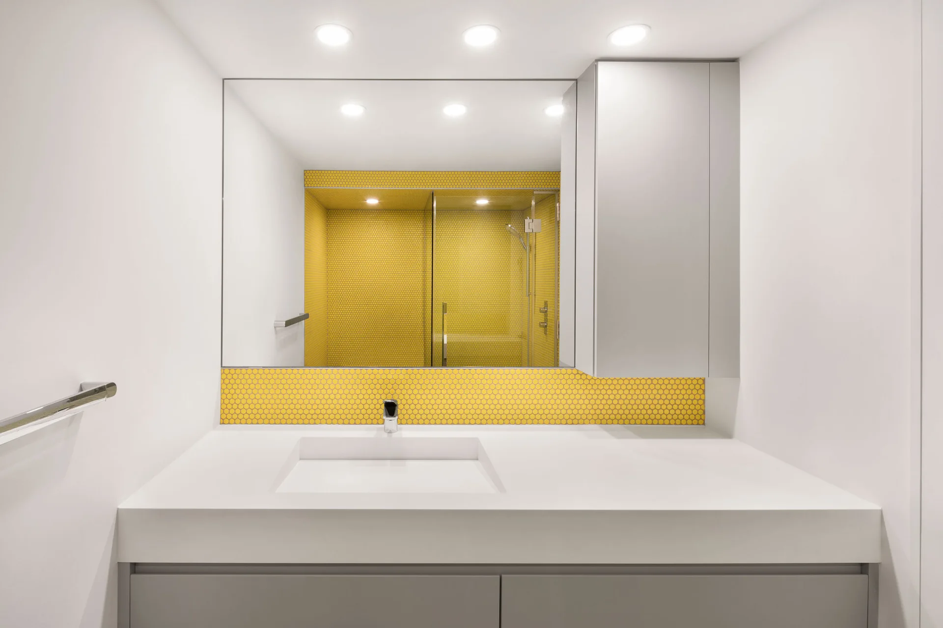 A modern bathroom featuring a white vanity with grey cabinetry, a large mirror, and a bright yellow hexagonal mosaic tile backsplash.