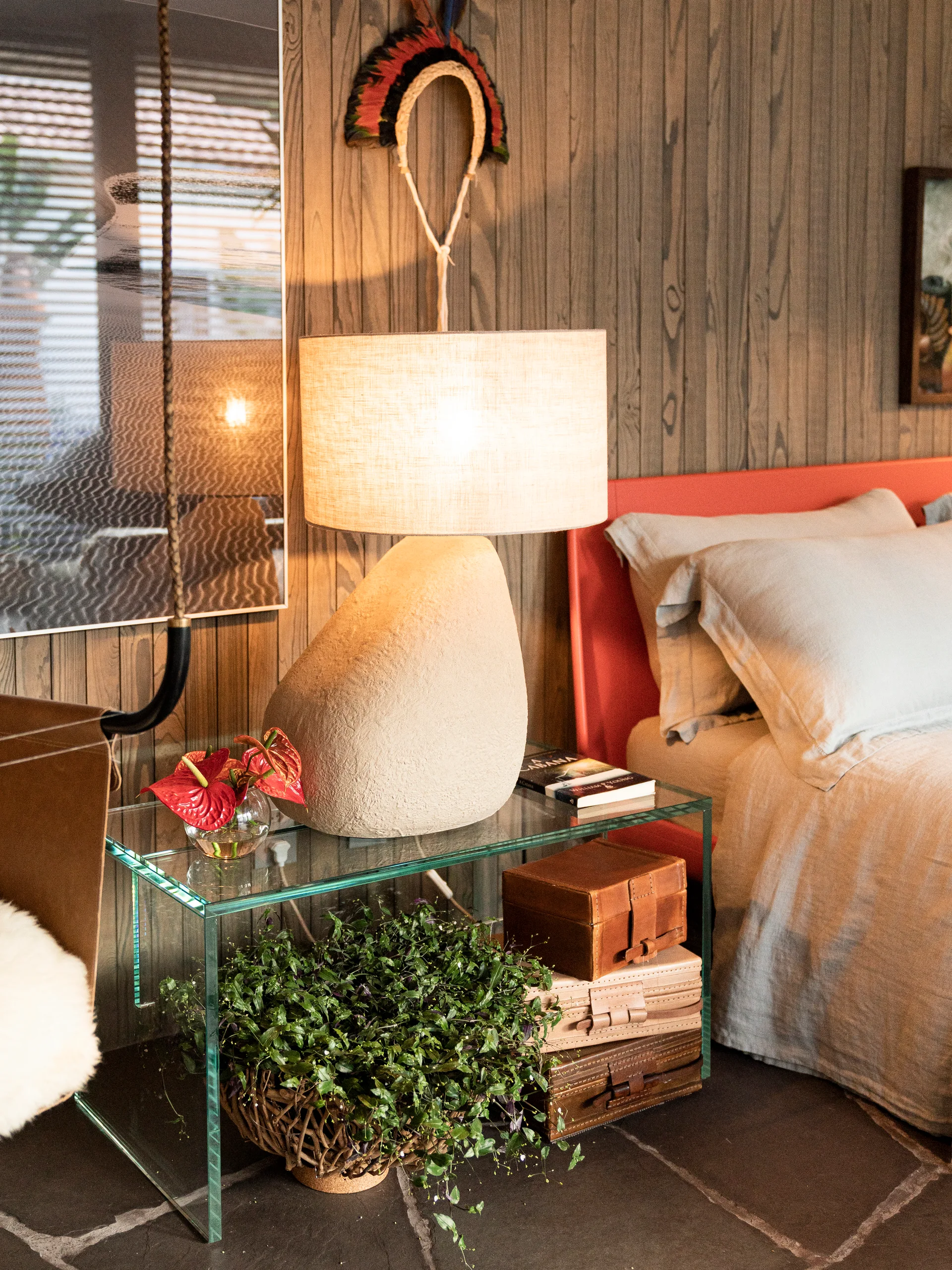 A bedroom corner features a textured stone lamp on a glass waterfall nightstand against a wood-paneled wall next to an orange headboard.