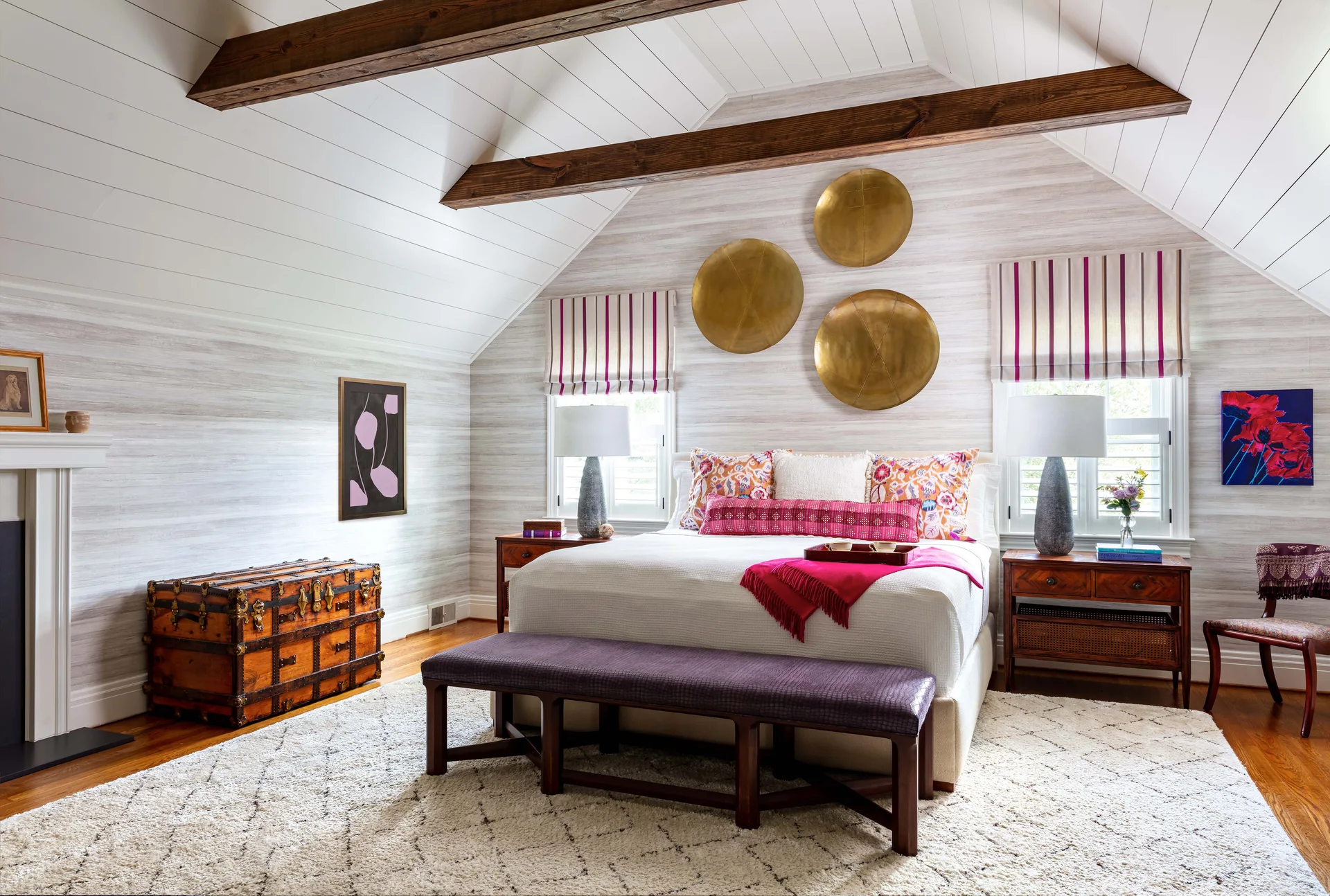 An eclectic bedroom with a vaulted beamed ceiling, brass disc wall art above the bed, a textured rug, and a vintage wooden trunk.