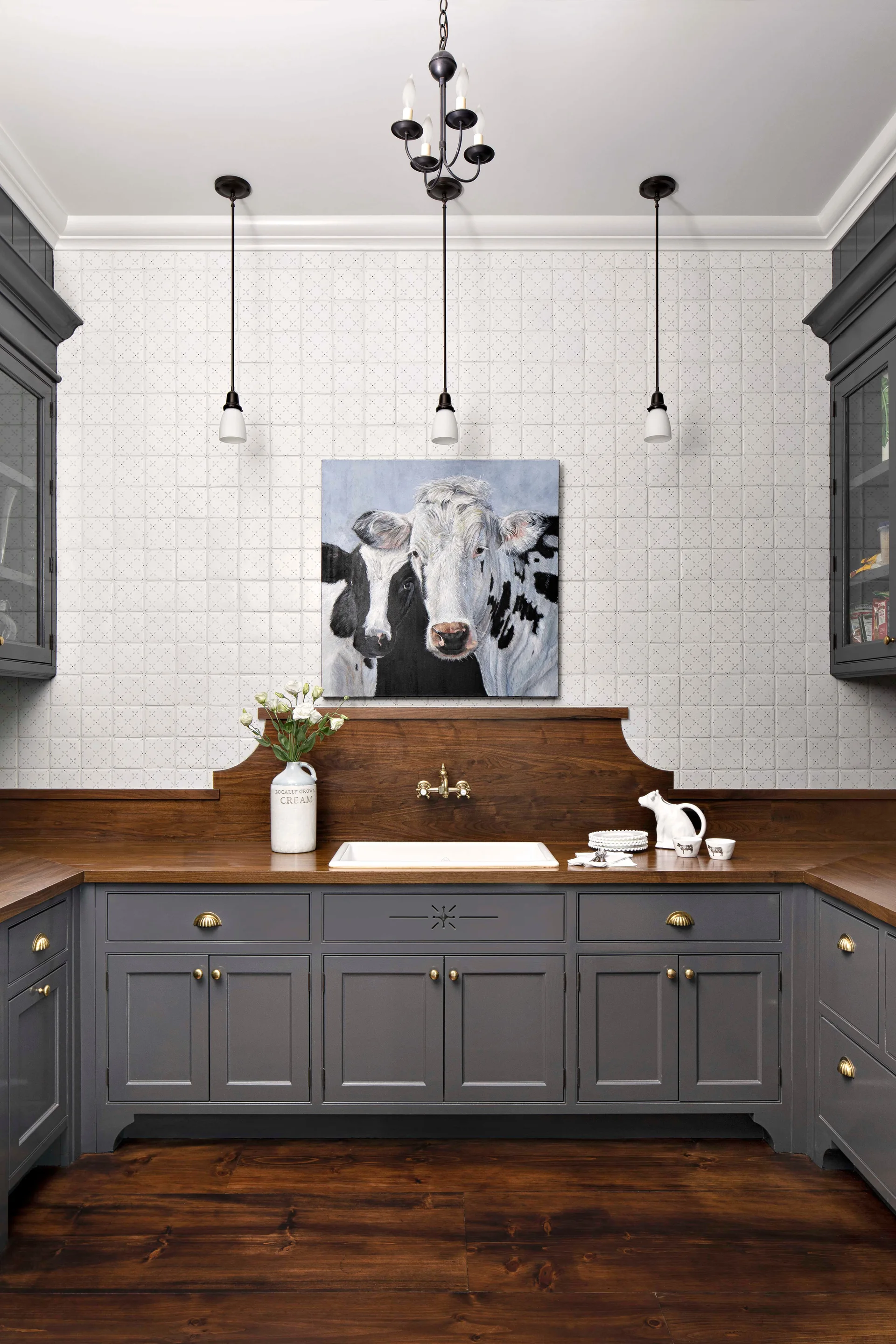 A kitchen scullery featuring grey shaker cabinets, a dark wood countertop, a white farmhouse sink, and a grid-tile wall with cow artwork.