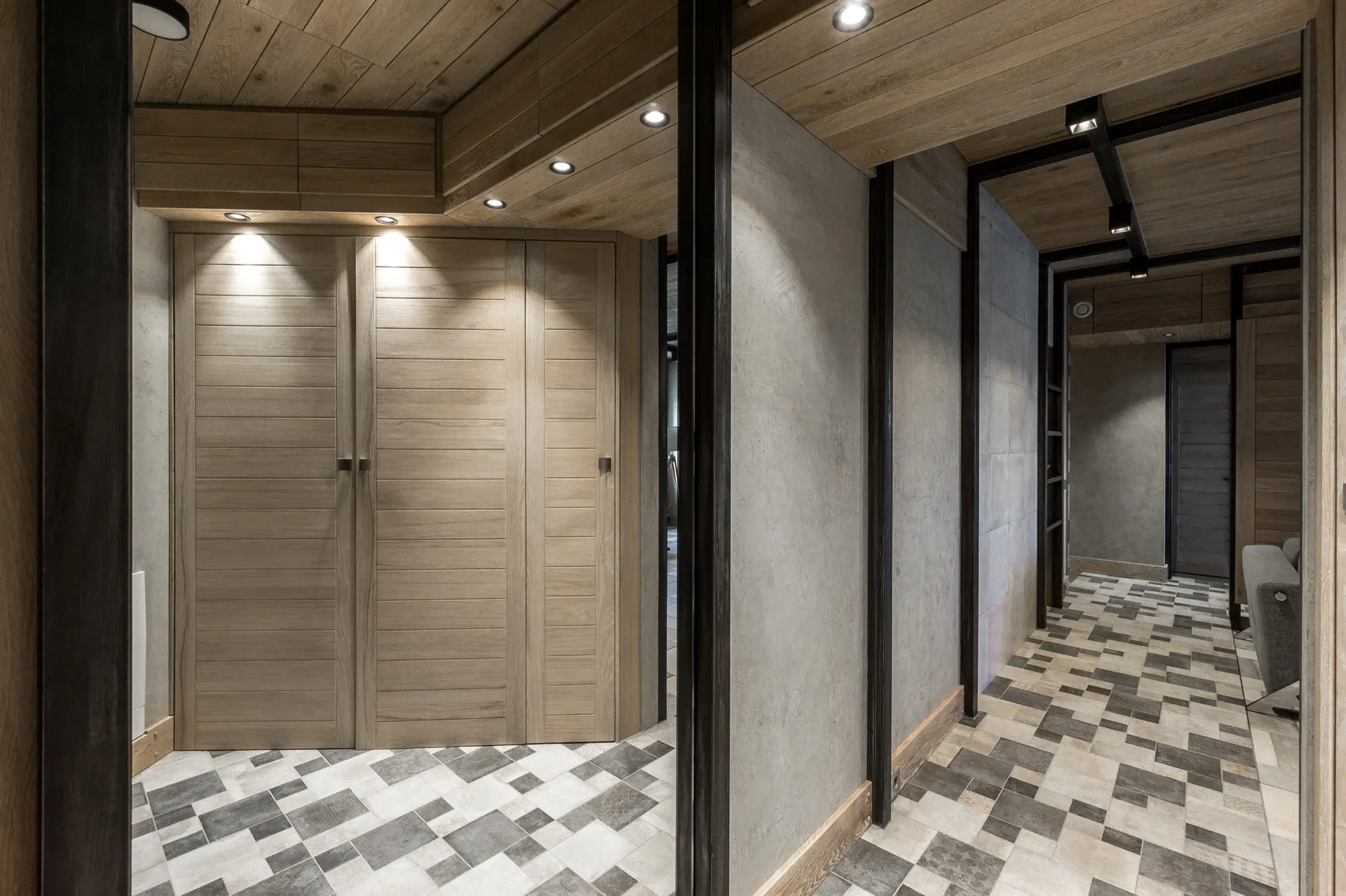 A modern hallway features light wood plank ceilings, concrete-look wall panels with black metal framing, and a checkered tiled floor.