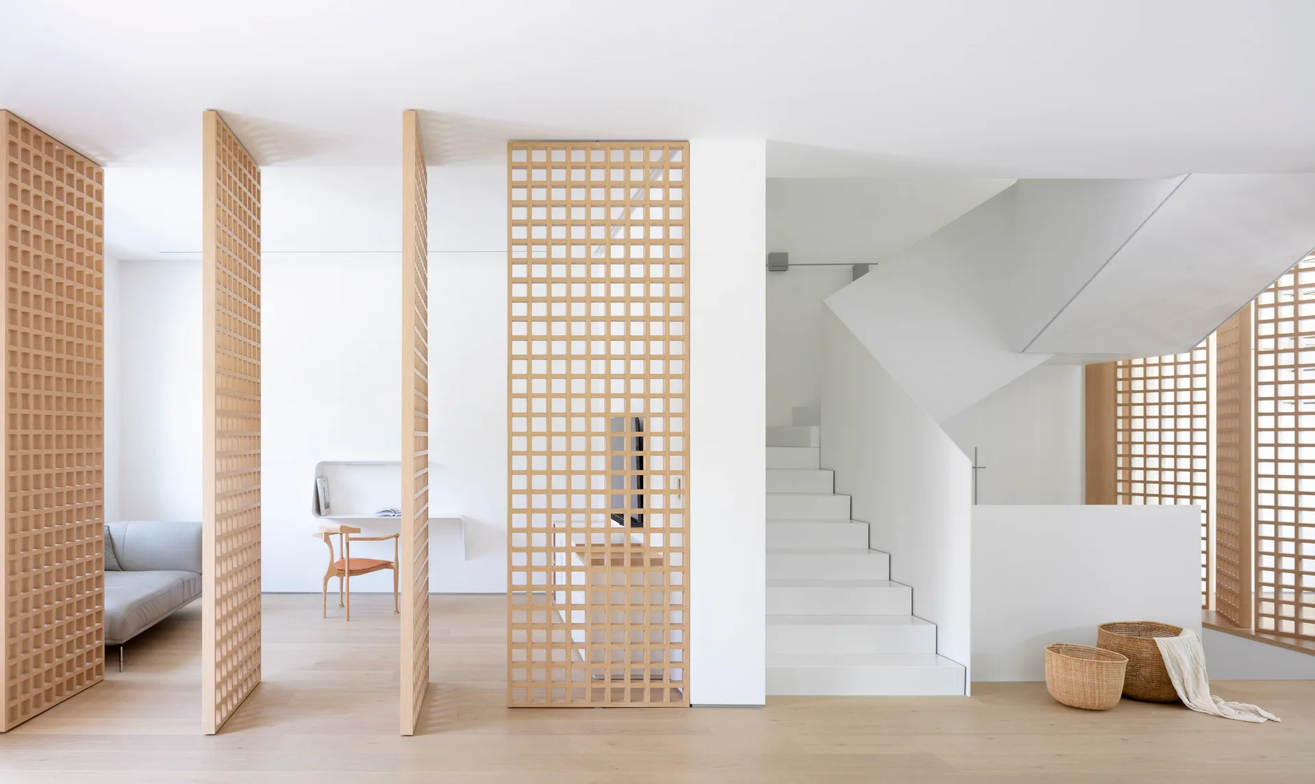 A minimalist interior featuring light oak grid partitions, a modern white staircase, wood floors, and a simple floating desk.