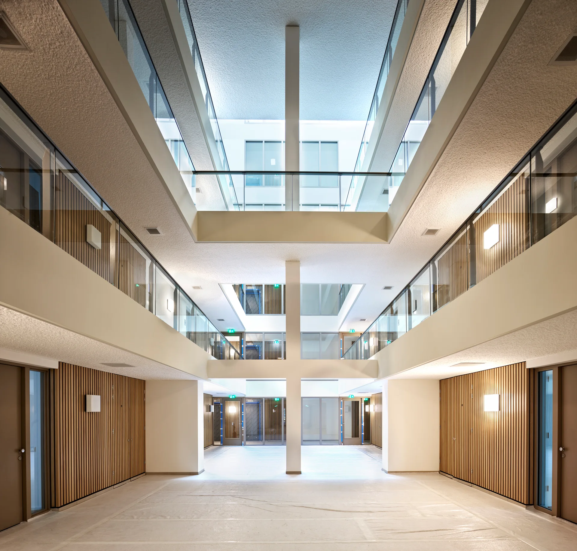A bright, multi-level modern atrium featuring vertical wood slat wall paneling, glass railings, off-white surfaces, and a central column.