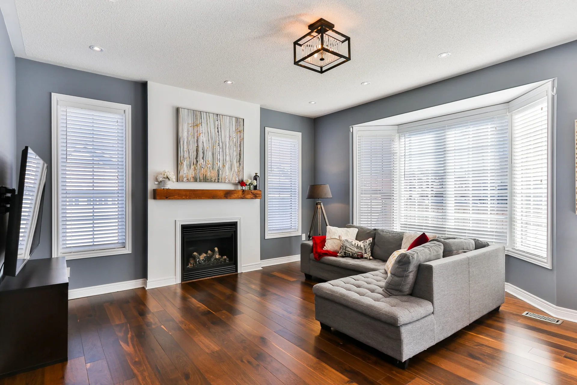 A contemporary living room featuring a grey sectional sofa, dark wood floors, and a fireplace with a chunky wood mantel.
