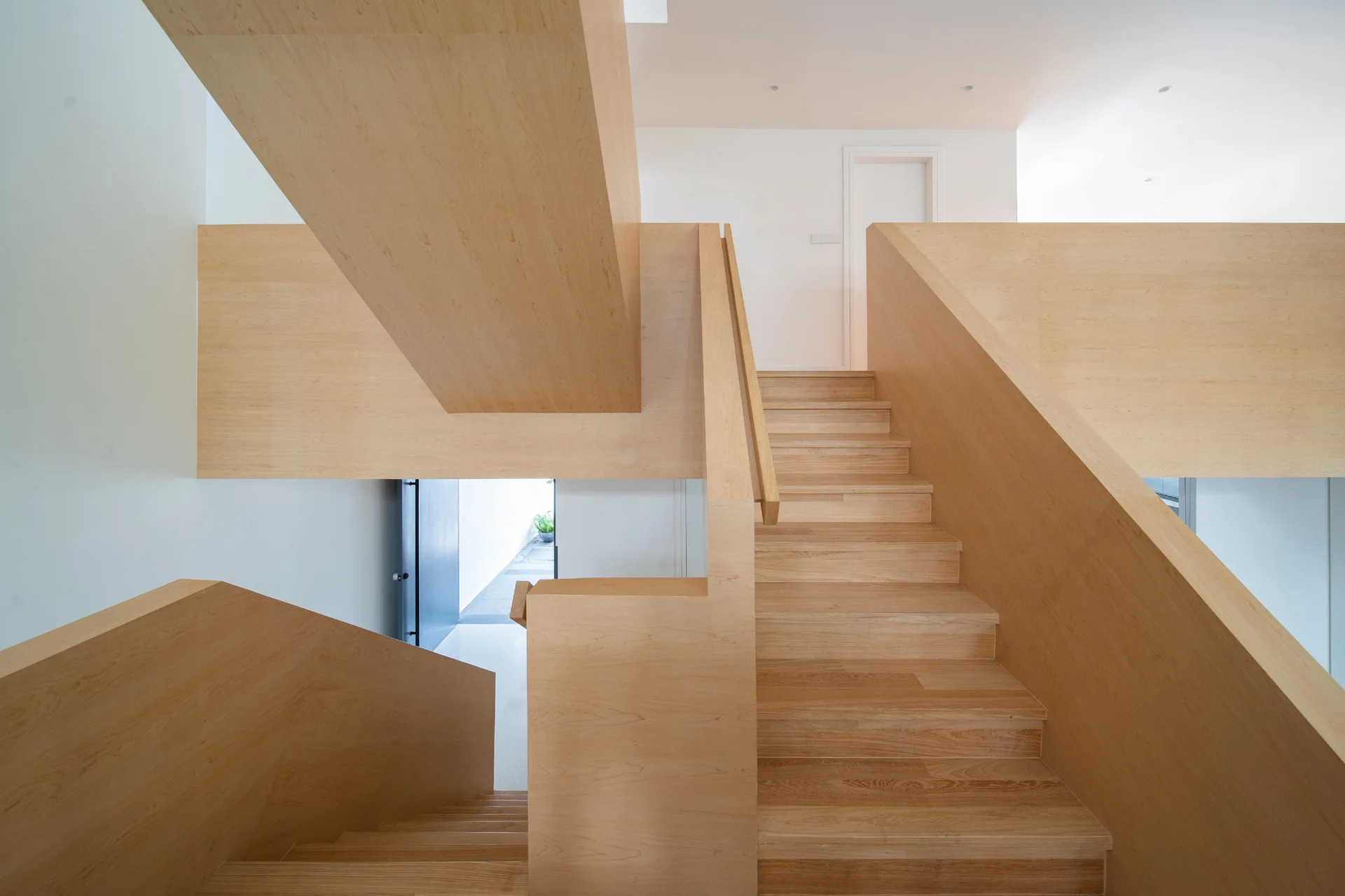 A minimalist residential staircase built from light wood features solid wood panel railings against flat white walls.