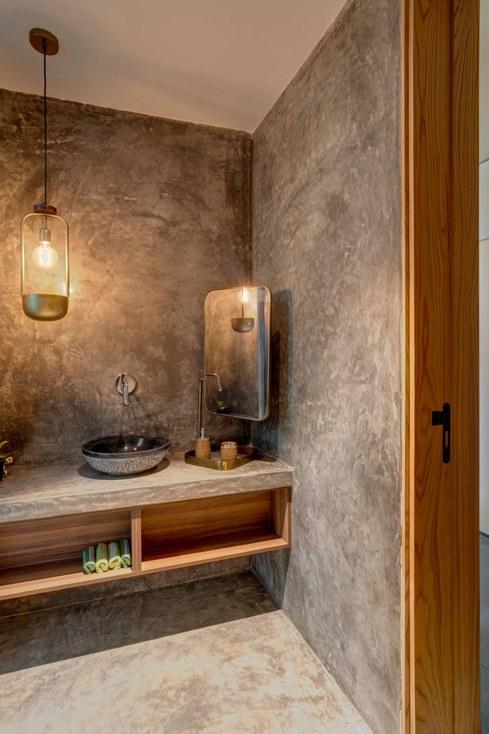 A minimalist gray concrete powder room with a vessel sink resting on a concrete vanity with open wood shelving underneath.