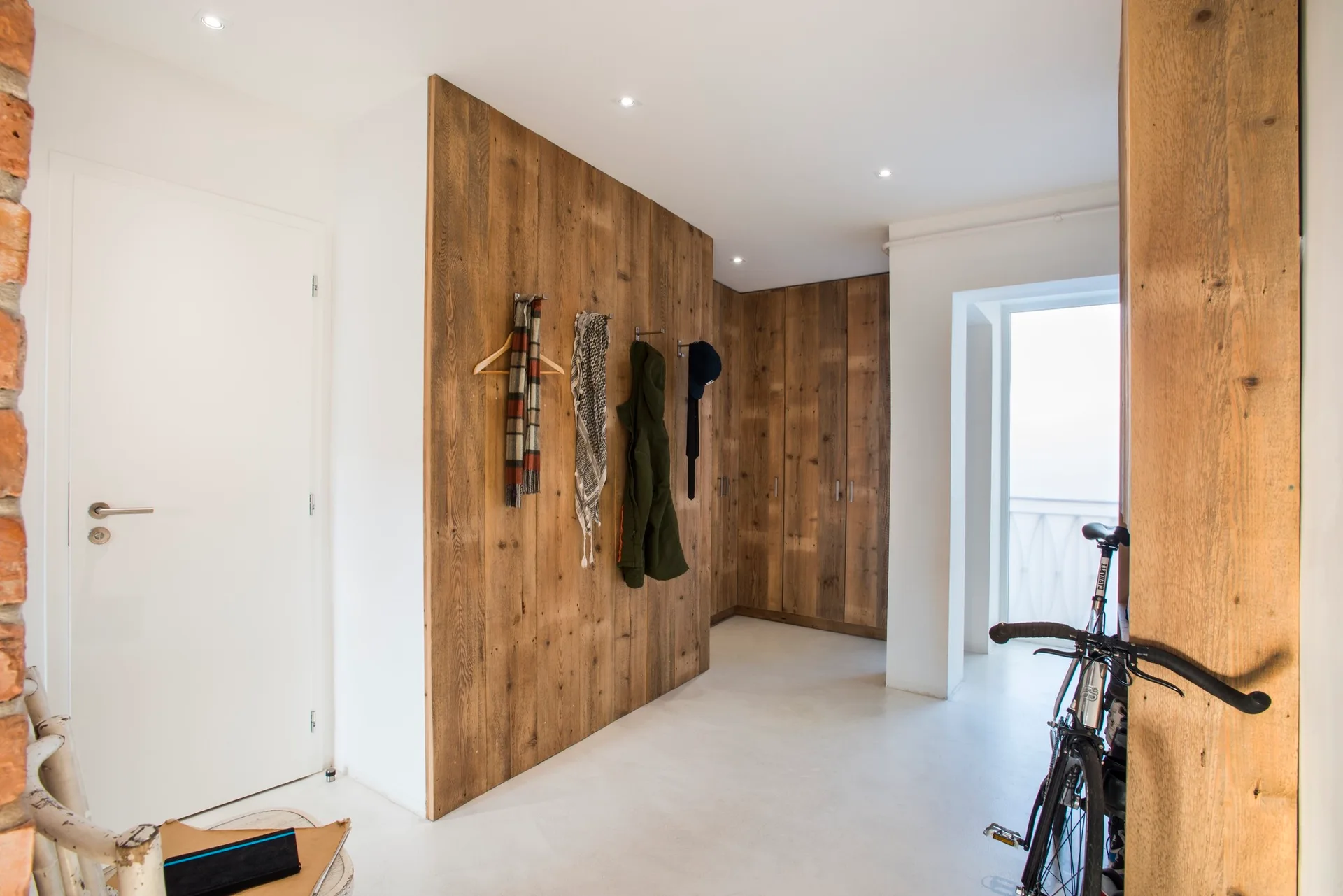 A minimalist mudroom hallway with vertical wood wall paneling, matching wood closet doors, and smooth white floors.
