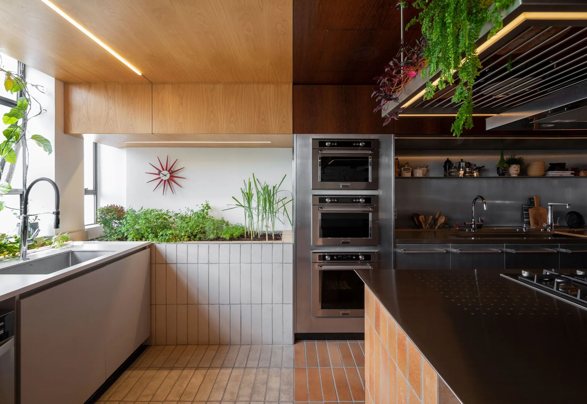 A modern kitchen featuring a dual-toned wood ceiling, a built-in vertical tiled planter filled with green plants, and stacked stainless steel wall ovens.