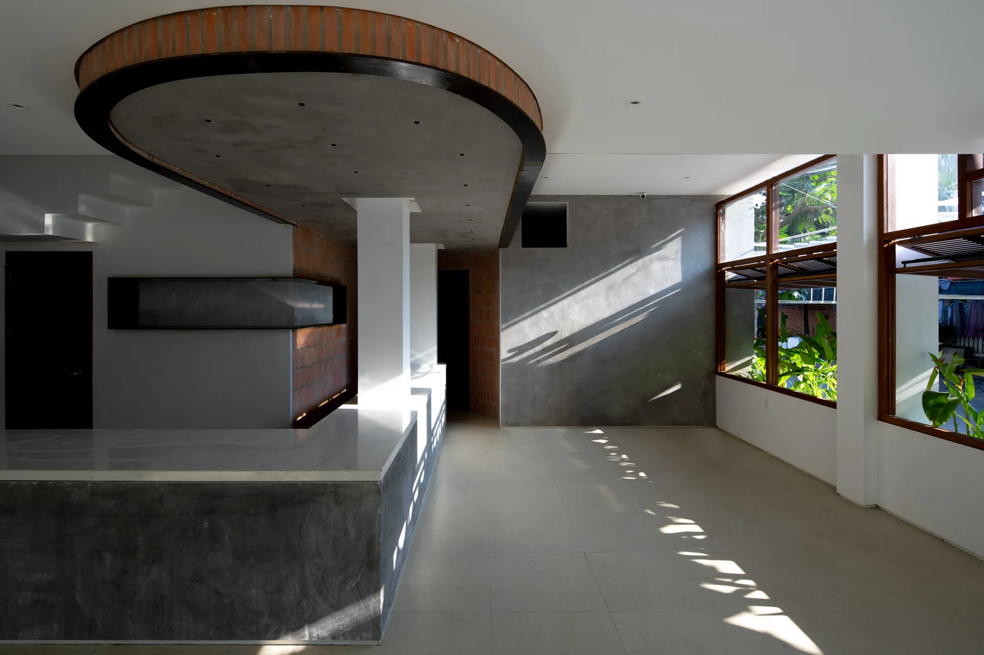 A minimalist interior space features a concrete counter, a unique curved ceiling with brick details, and sunlight casting shadows across the floor.