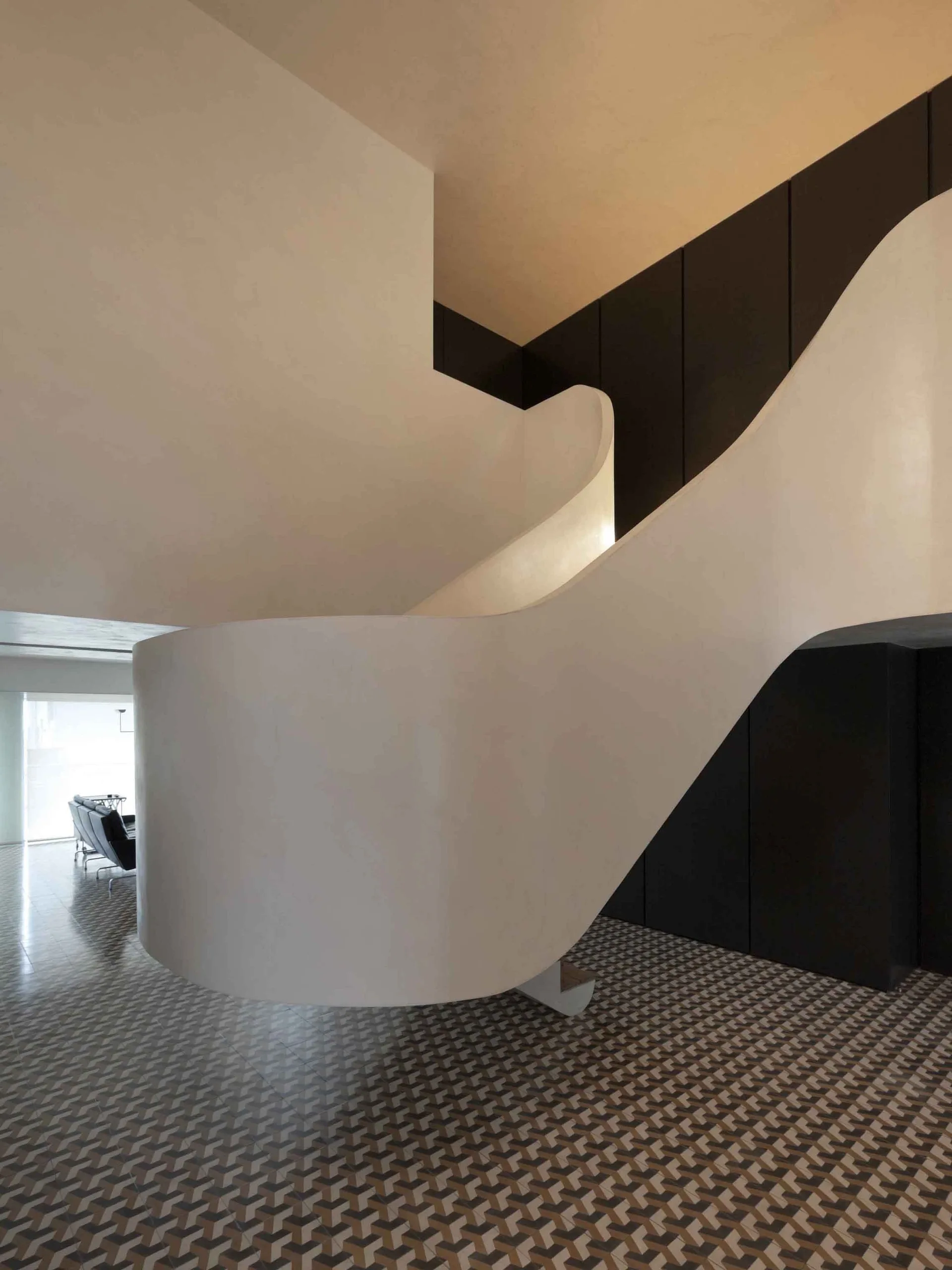 A curved white sculptural staircase winds down onto a floor with geometric cube-patterned tiles in a modern interior.