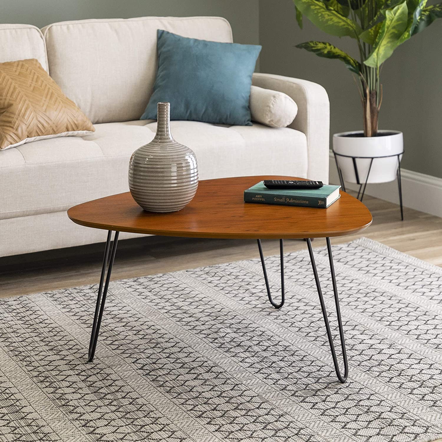 A triangular wooden coffee table with hairpin legs sits on a geometric patterned rug in front of a cream sofa.