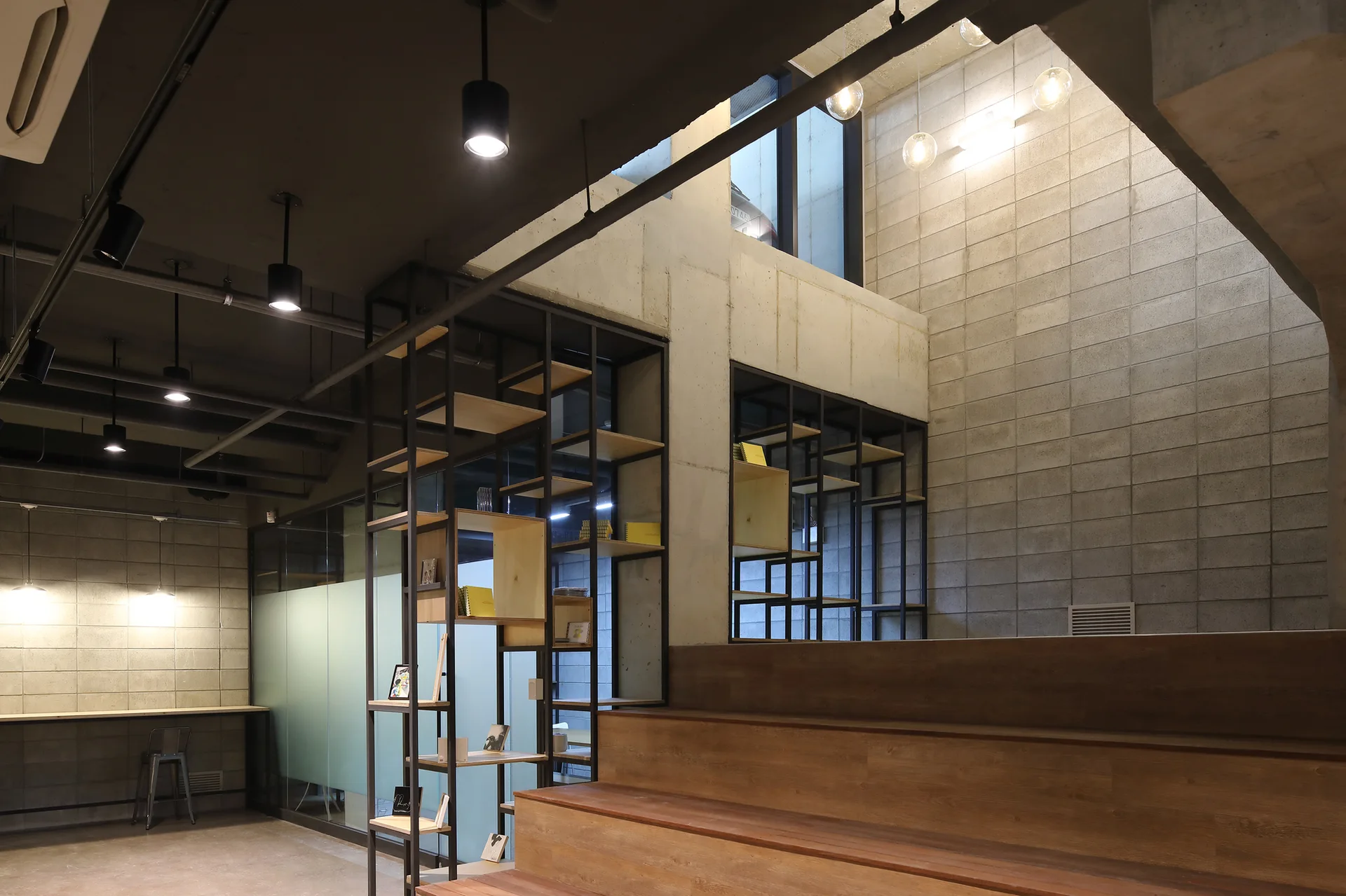 An industrial interior featuring a wide wooden staircase next to black metal grid shelving and exposed concrete block walls.
