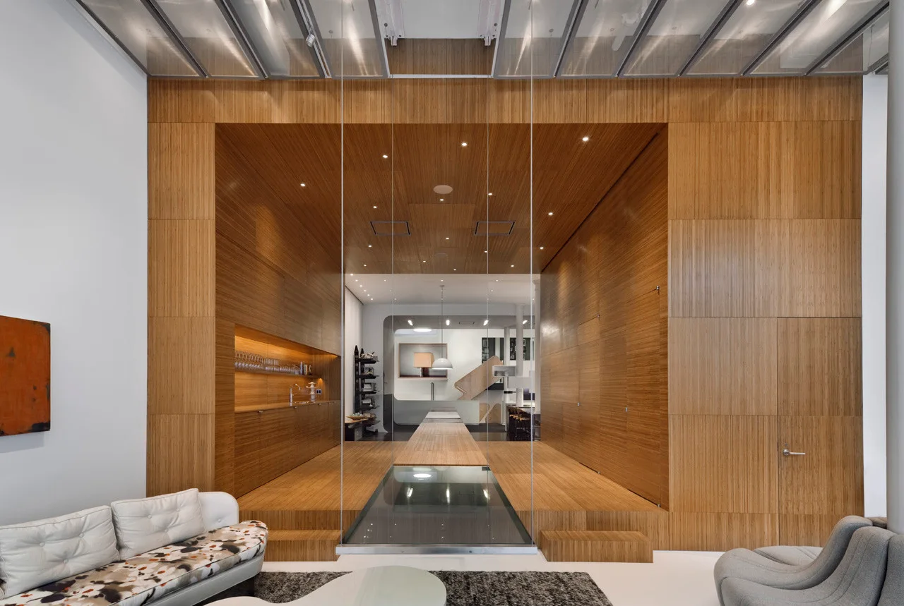 A modern living space featuring a raised wooden platform and matching paneling behind a tall glass partition.