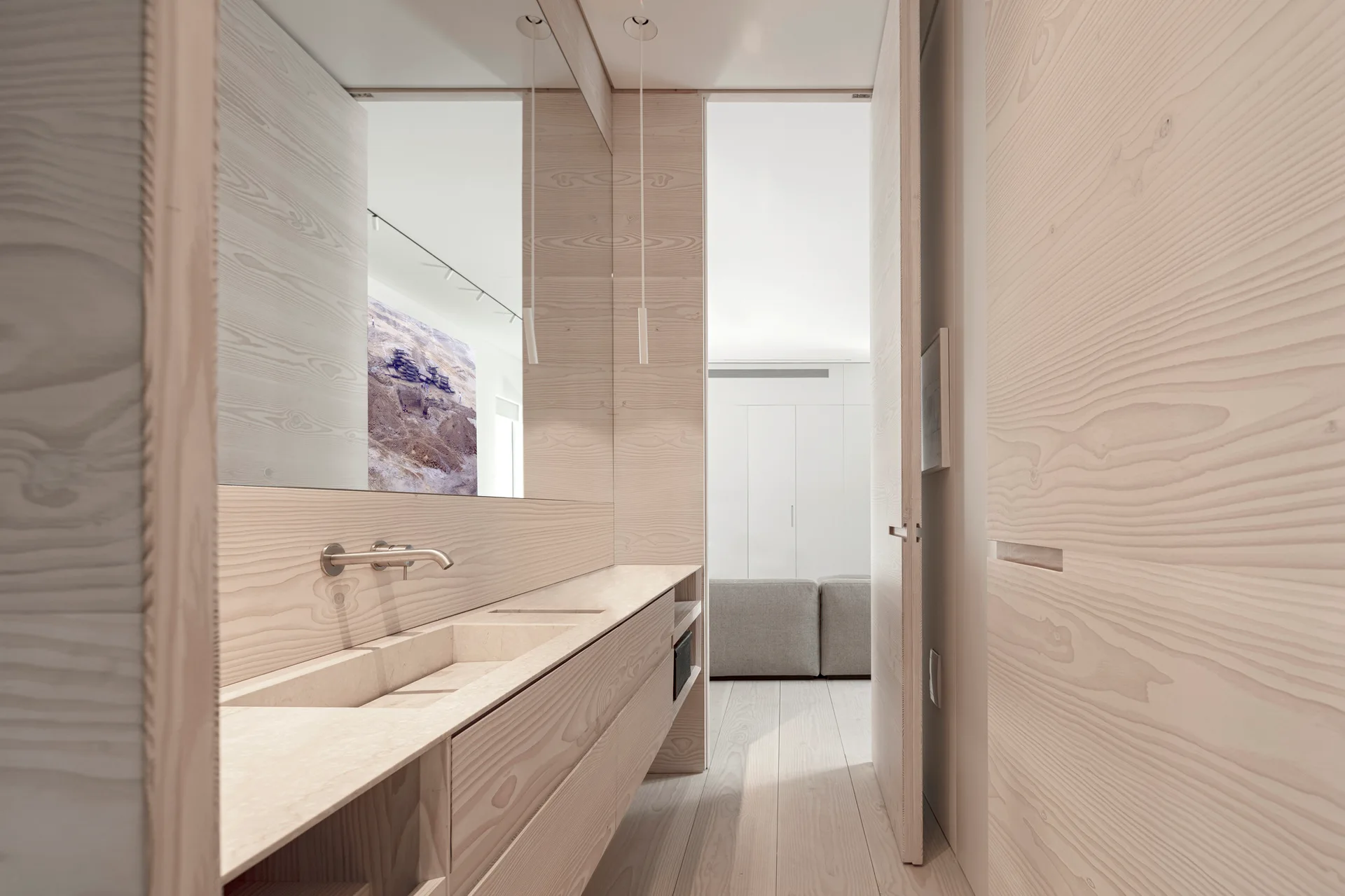 A minimalist bathroom vanity area with light wood paneling, an integrated beige stone sink basin, a wall-mounted faucet, and a large mirror.