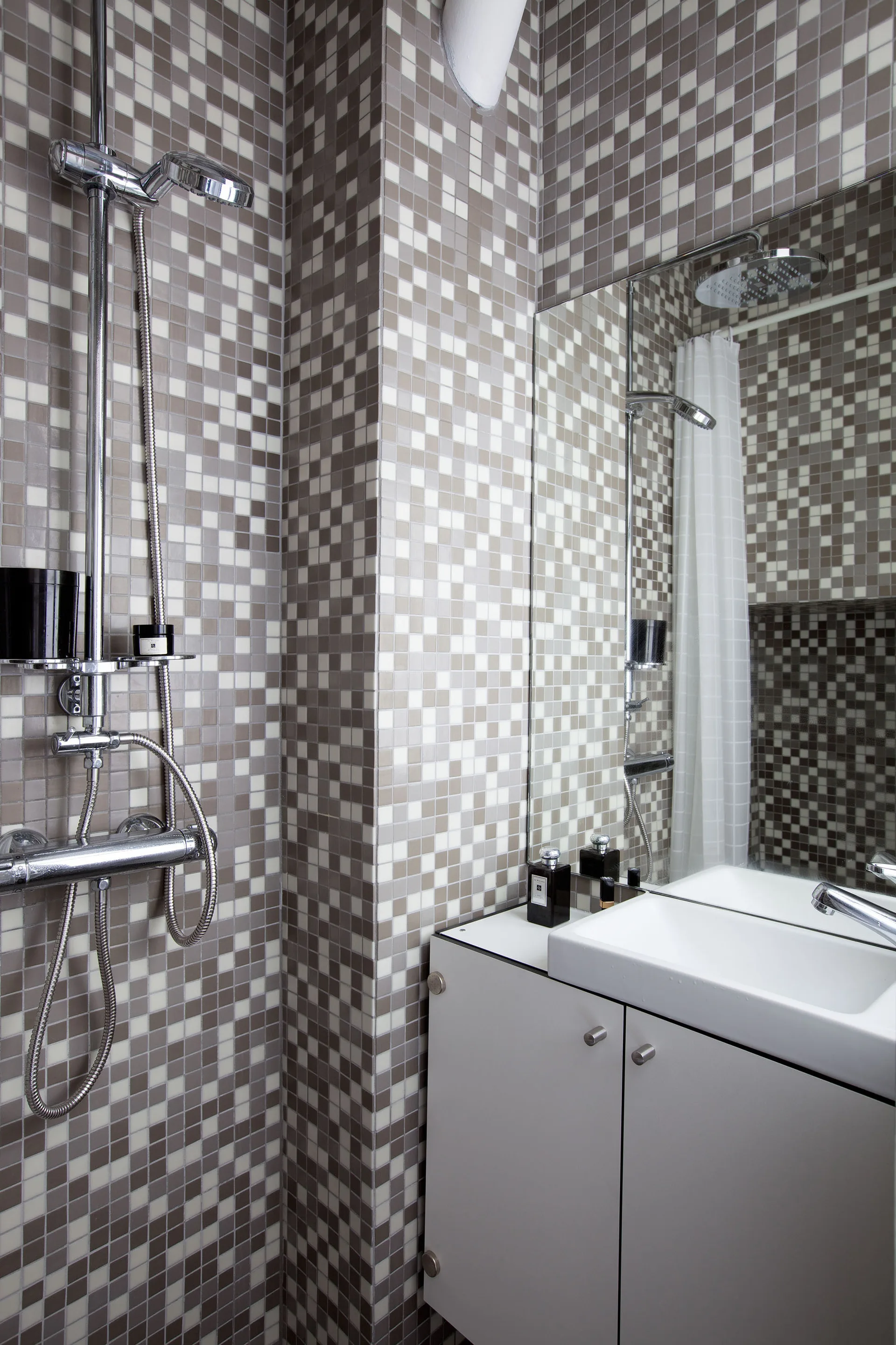 A bathroom features grey and white checkered mosaic wall tiles, a sleek white vanity with a rectangular mirror, and a chrome shower fixture.