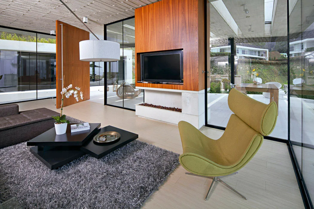 A modern living room featuring floor-to-ceiling glass walls, a gray shag rug, a tiered black coffee table, and a sculptural lime green accent chair.