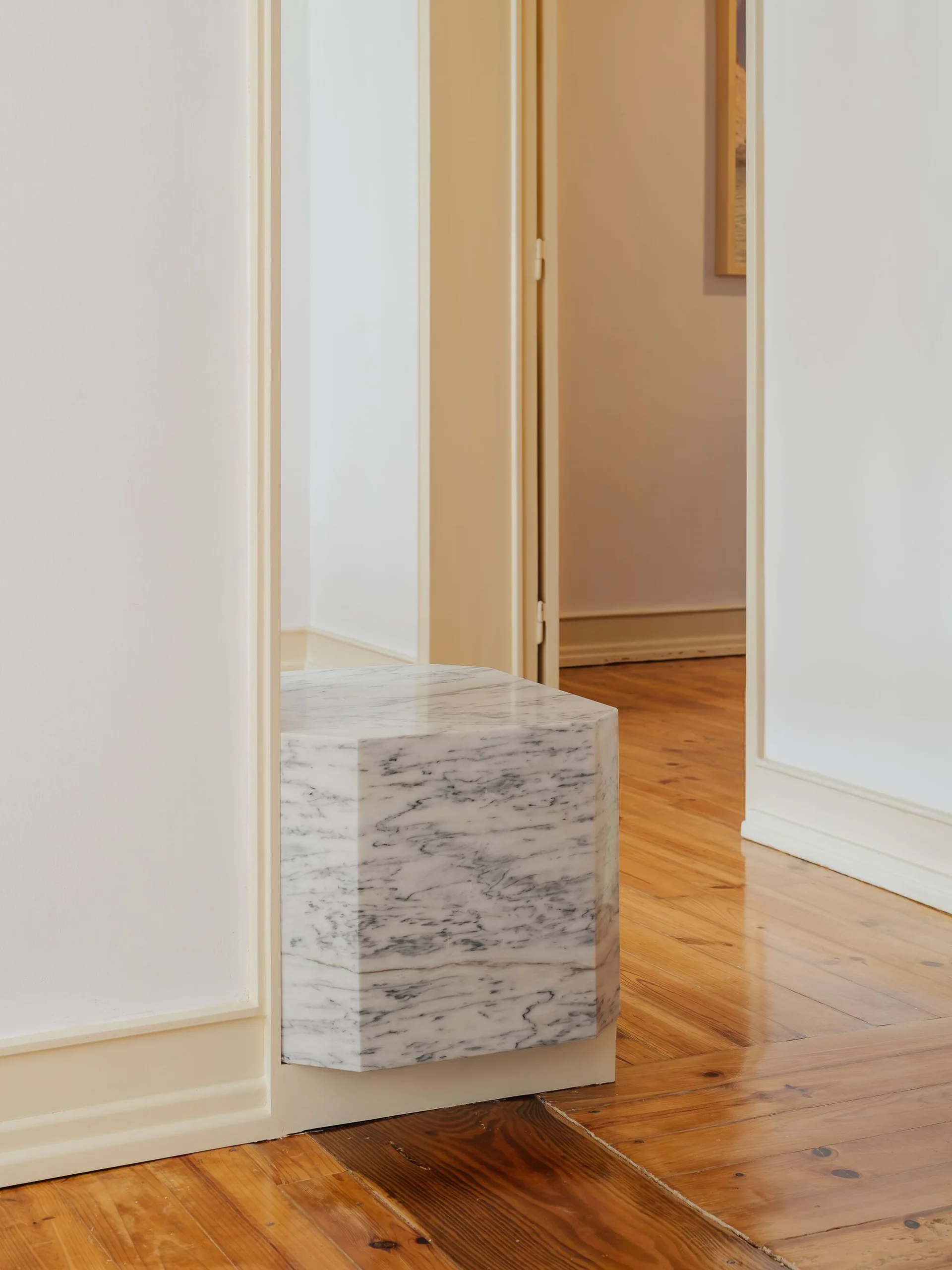 A hexagonal white marble pedestal with grey veining is built into a cream doorframe above polished wood flooring.