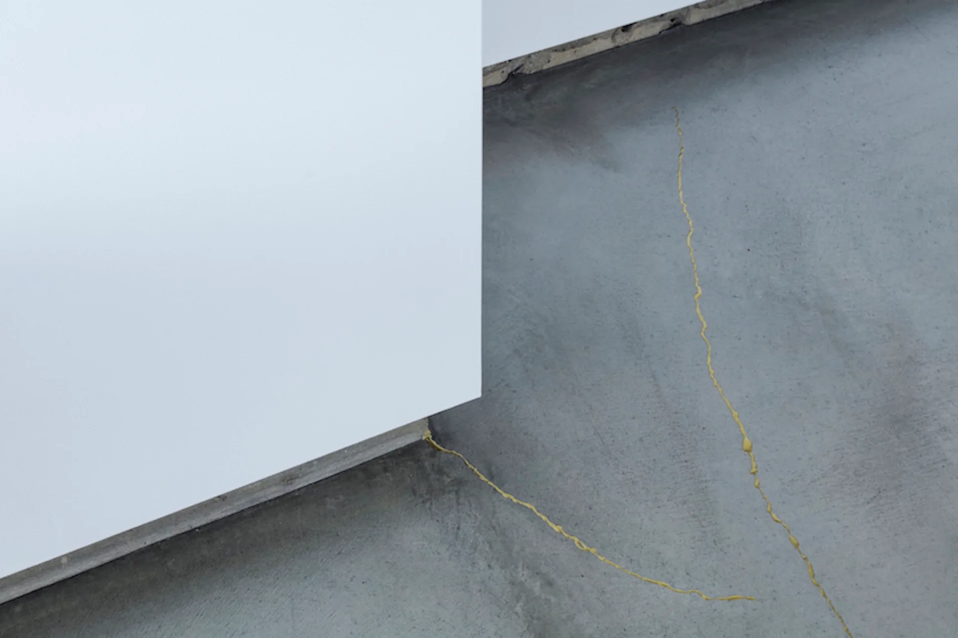 A close-up of a smooth white wall corner meeting a grey concrete floor with bright yellow sealant filling the cracks.