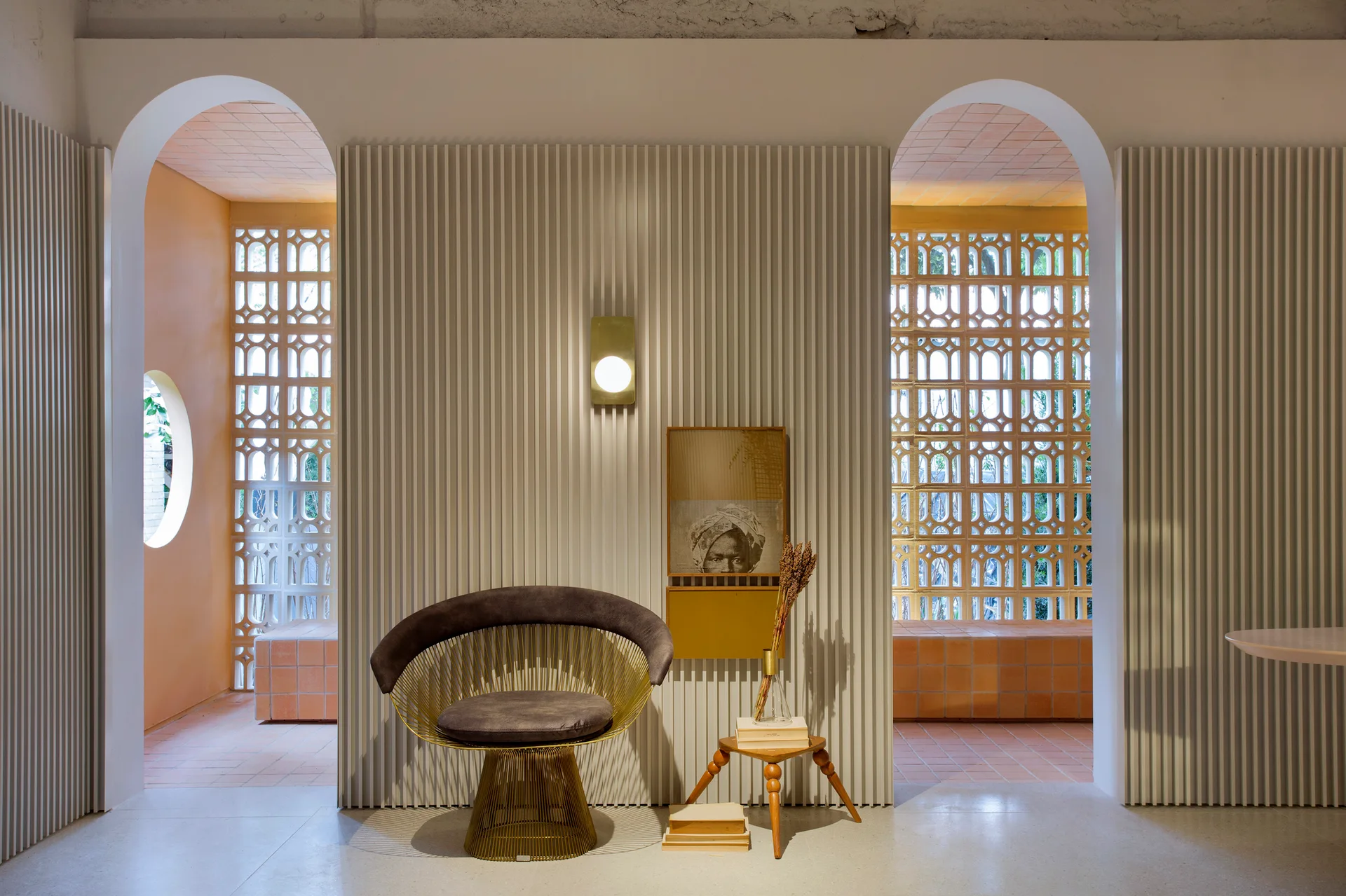 A fluted accent wall with two arched openings reveals terracotta breeze block screens behind a wire accent chair and wooden side table.