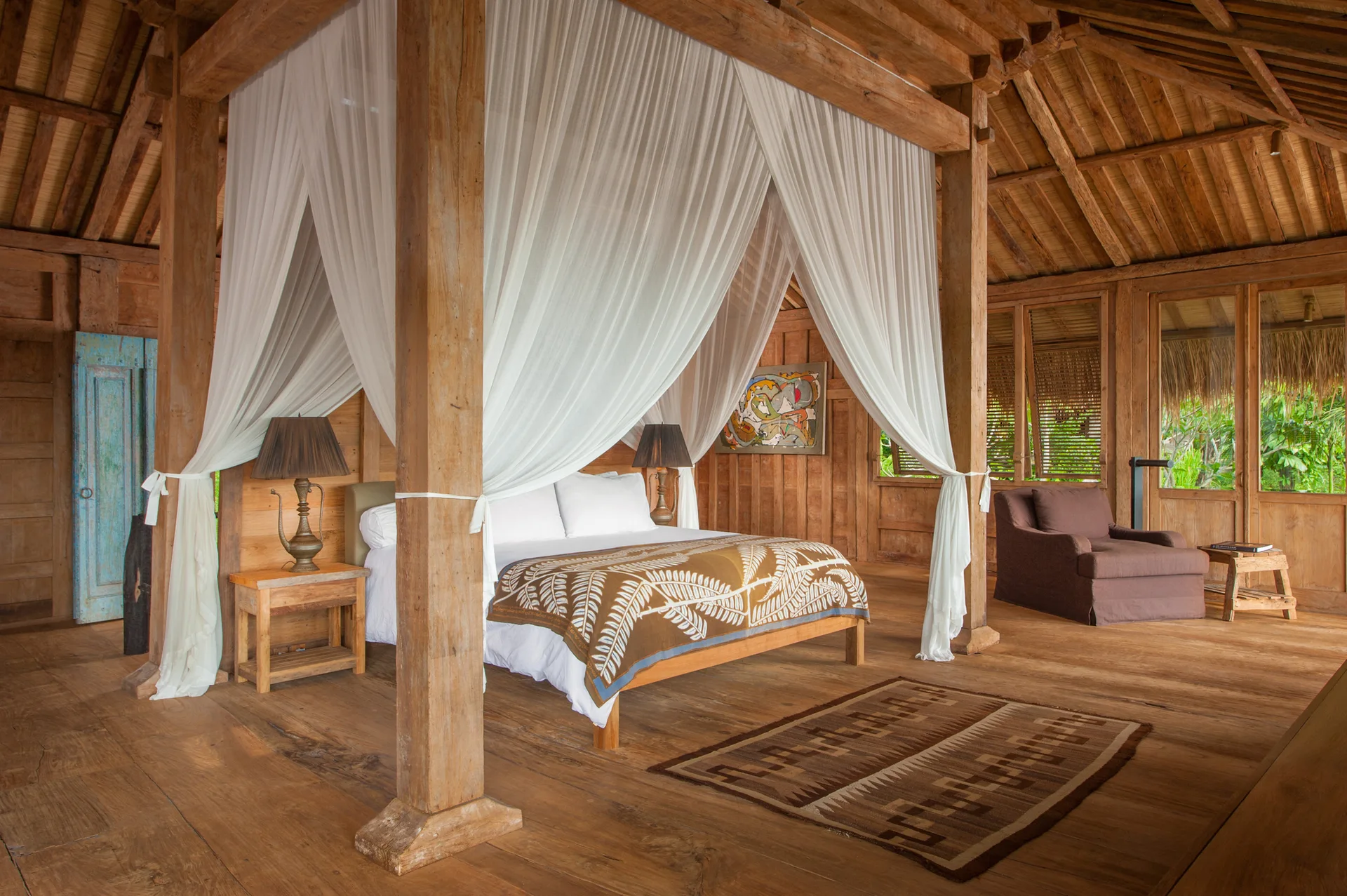 A rustic all-wood bedroom featuring a large timber canopy bed draped in sheer white curtains, flanked by natural wood nightstands under a vaulted ceiling.