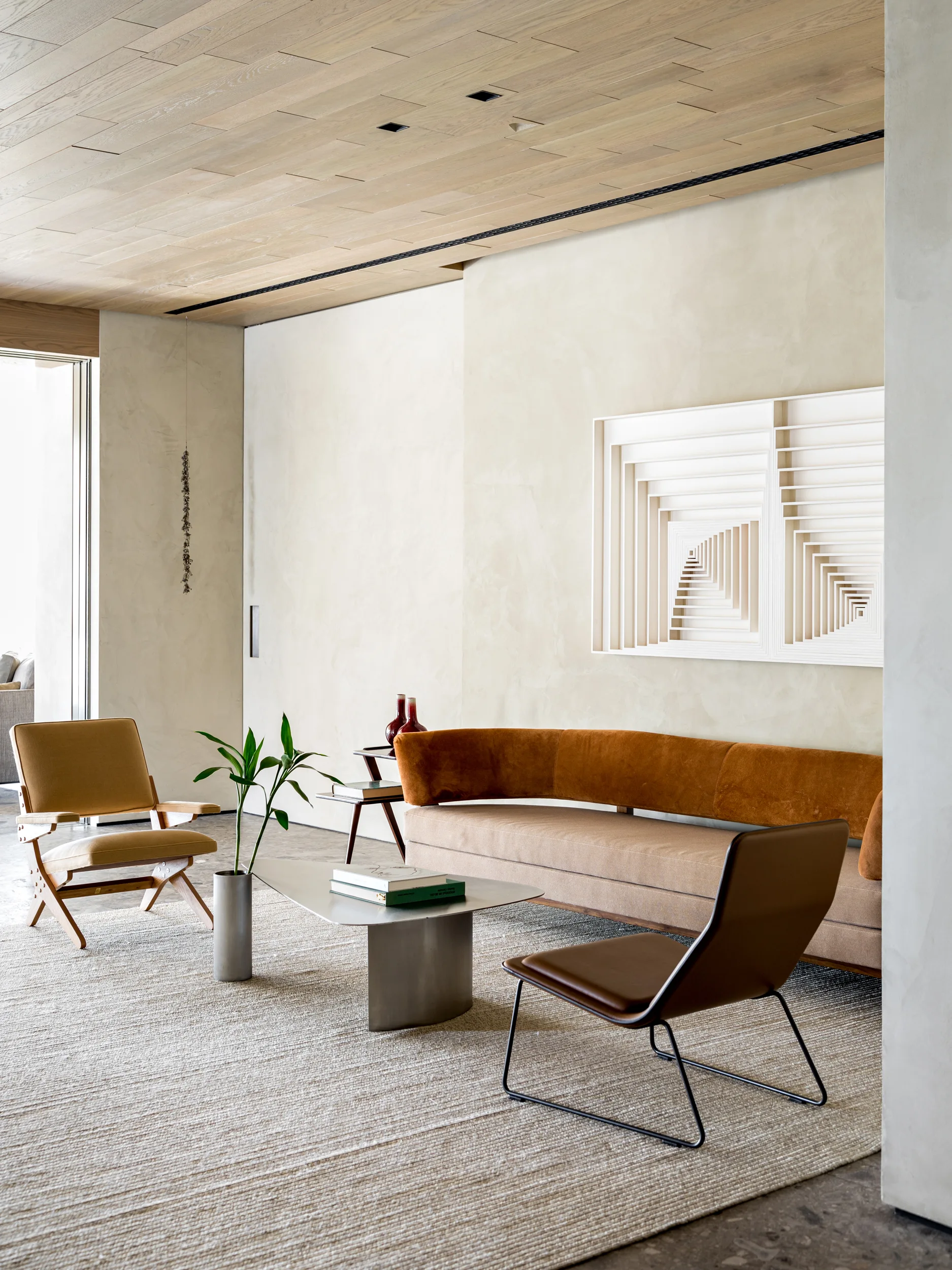 A modern living room features a curved orange and tan sofa, geometric wall art, and leather chairs under a light wood plank ceiling.